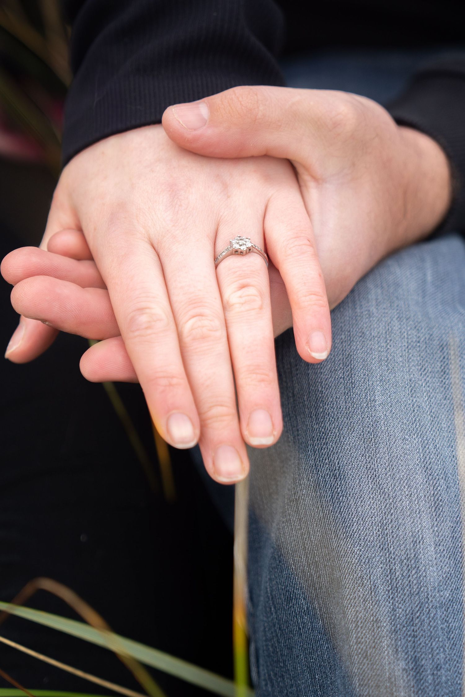 A close-up view of hands resting on denim jeans accompanied by a delicate engagement ring.