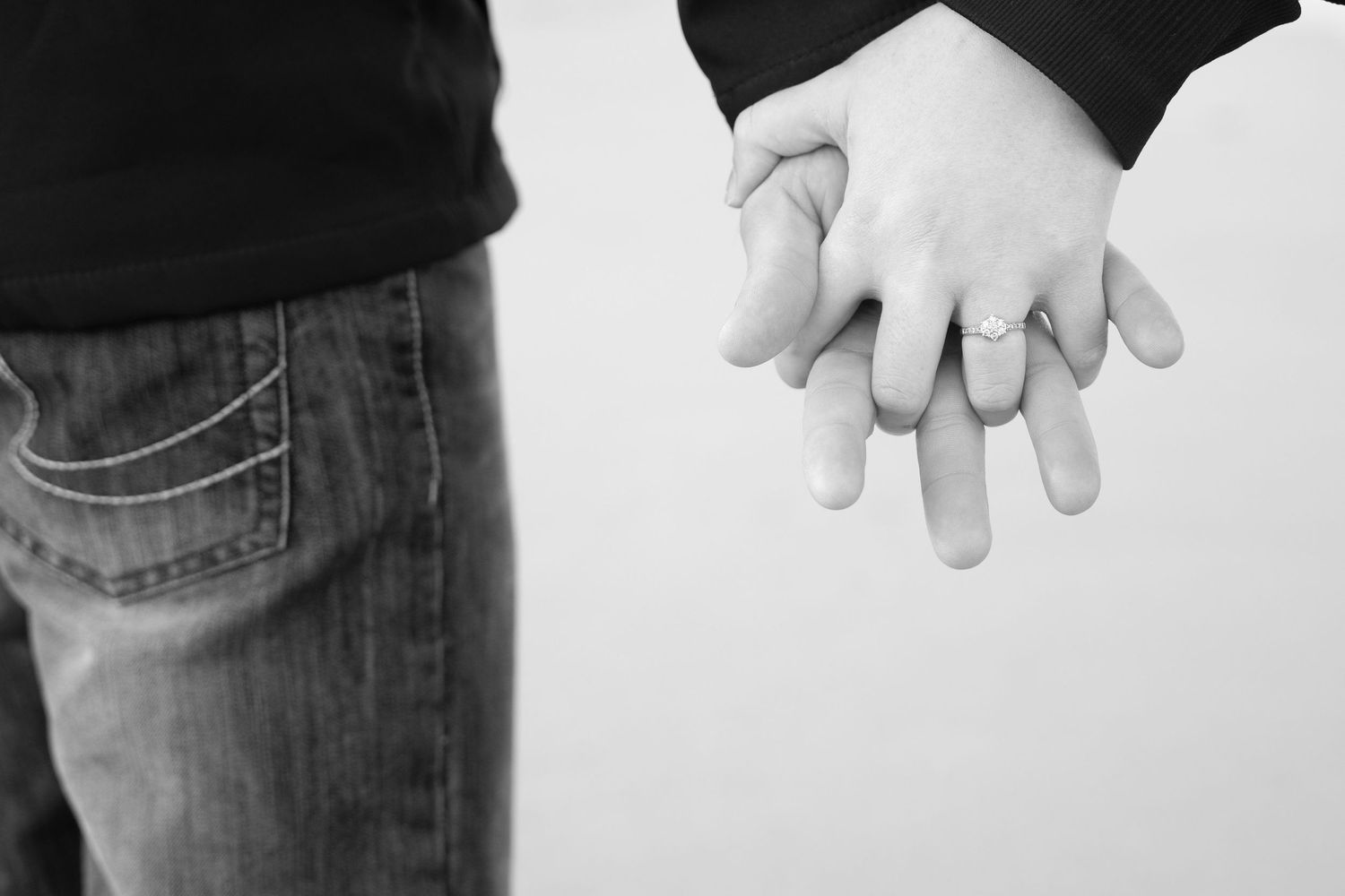 Close-up black and white photo of two people holding hands intimately against a white background.