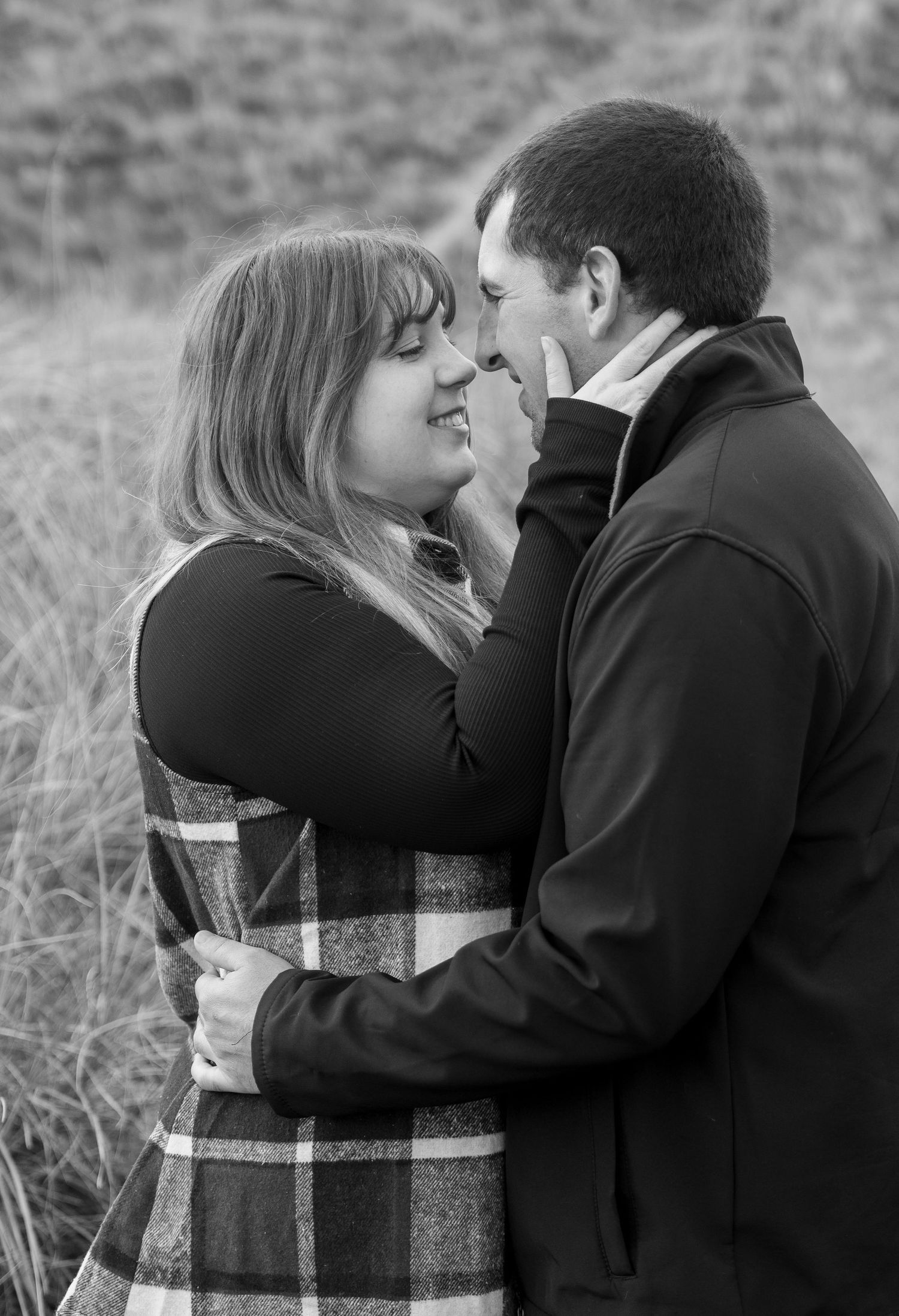 Romantic black and white portrait of a couple embracing in a field wearing winter coats.