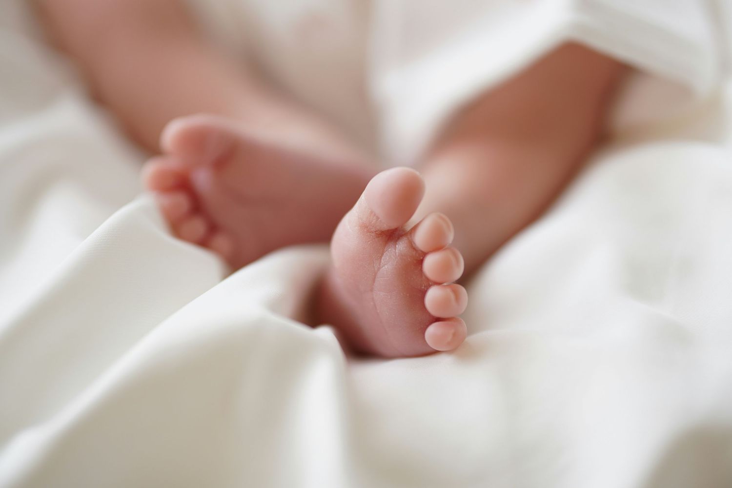 Close-up view of tiny baby feet against soft white fabric.