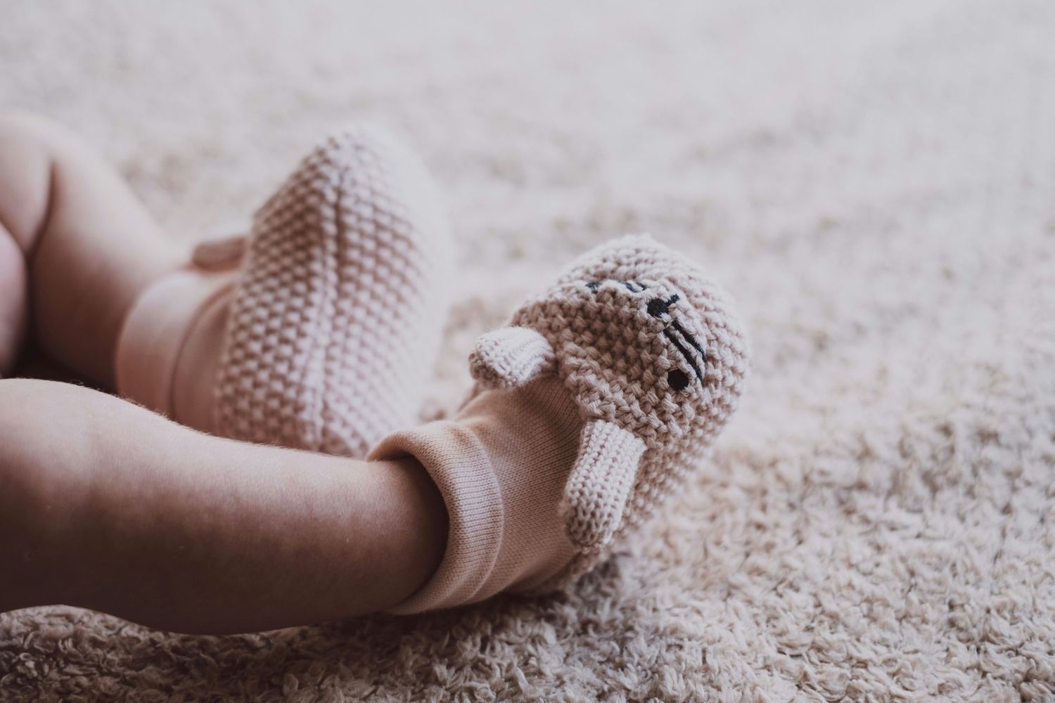 Close-up of tiny knitted baby bootie on textured carpet.