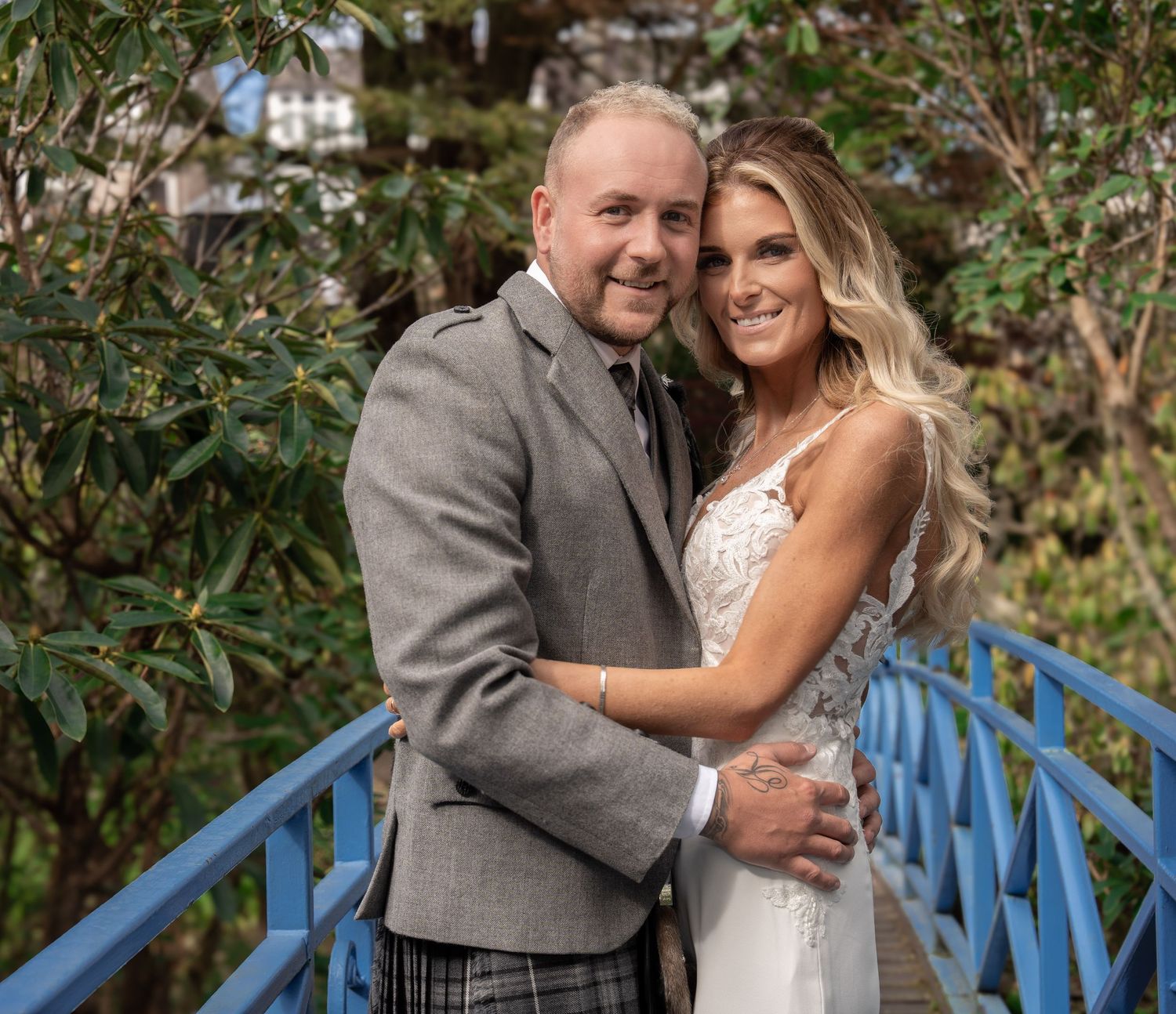 Couple sharing romantic moment on blue bridge surrounded by greenery.