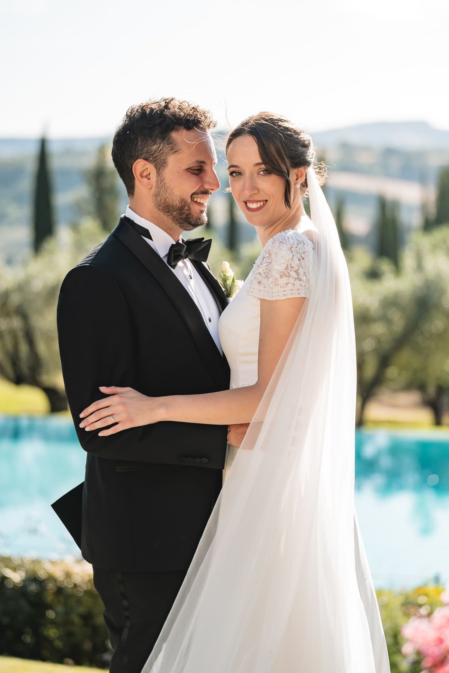 Abbraccio degli sposi tra gli ulivi accanto alla piscina dell'Antica Fattoria Paterno, Toscana