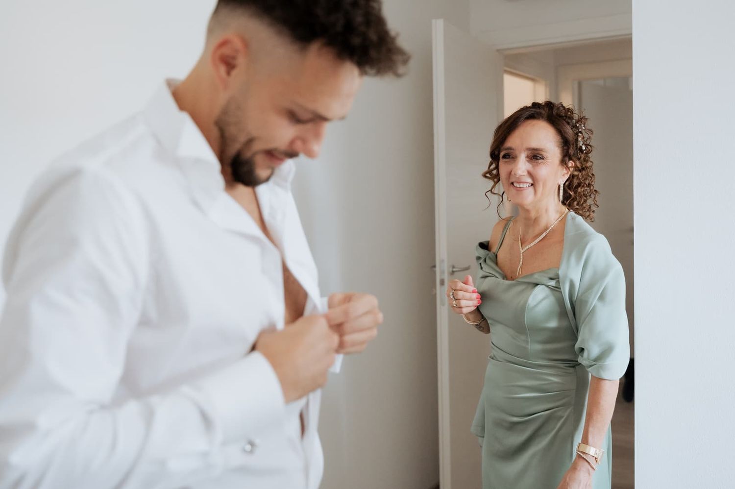 Lo sposo si abbottona la camicia accanto a una familiare durante i preparativi, matrimonio in Toscana
