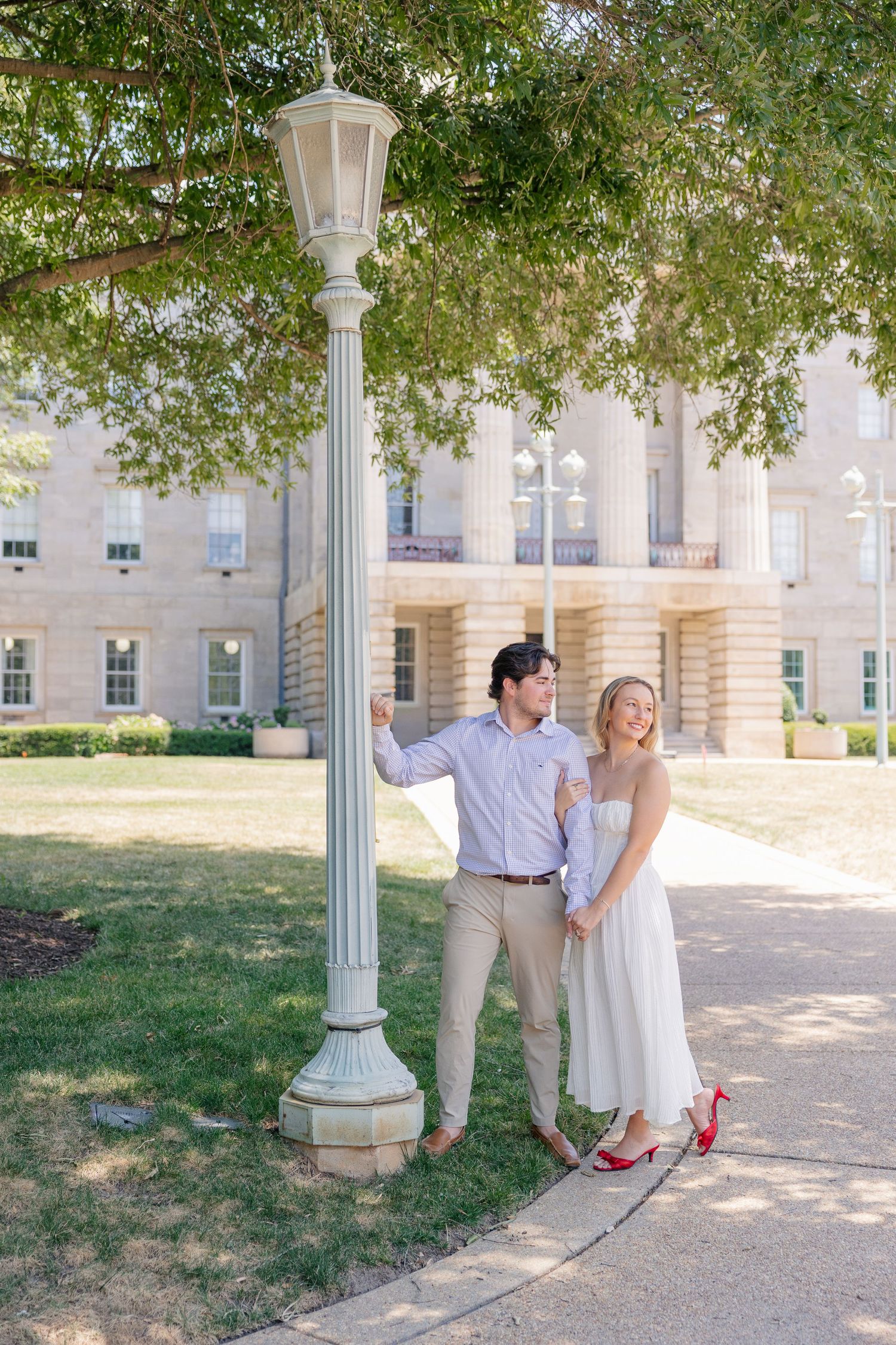 Happy couple posing by a vintage lamppost with a grand columned building in the background, engagement session.