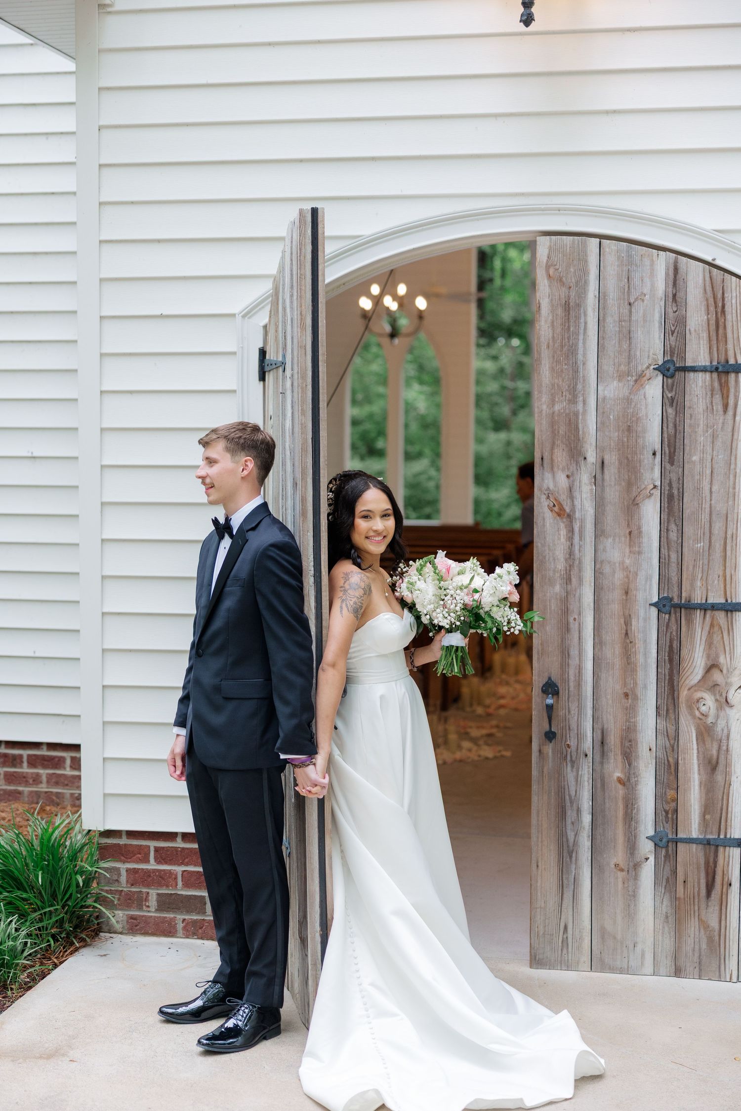 Elegant wedding portraits captured in front of a white chapel with rustic wooden doors.