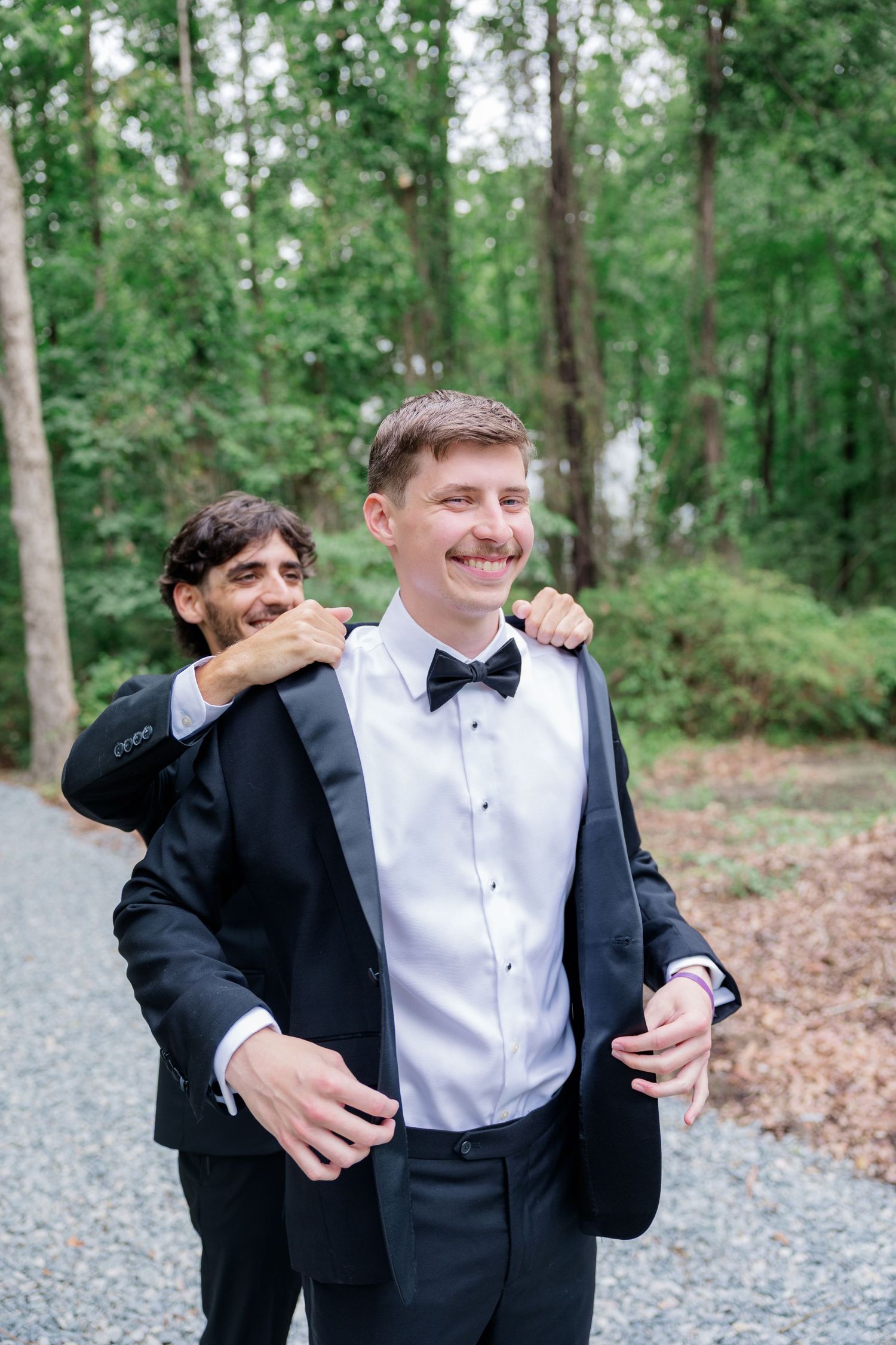 Groomsmen sharing laughs and playful moments in formal attire at an outdoor wedding venue.