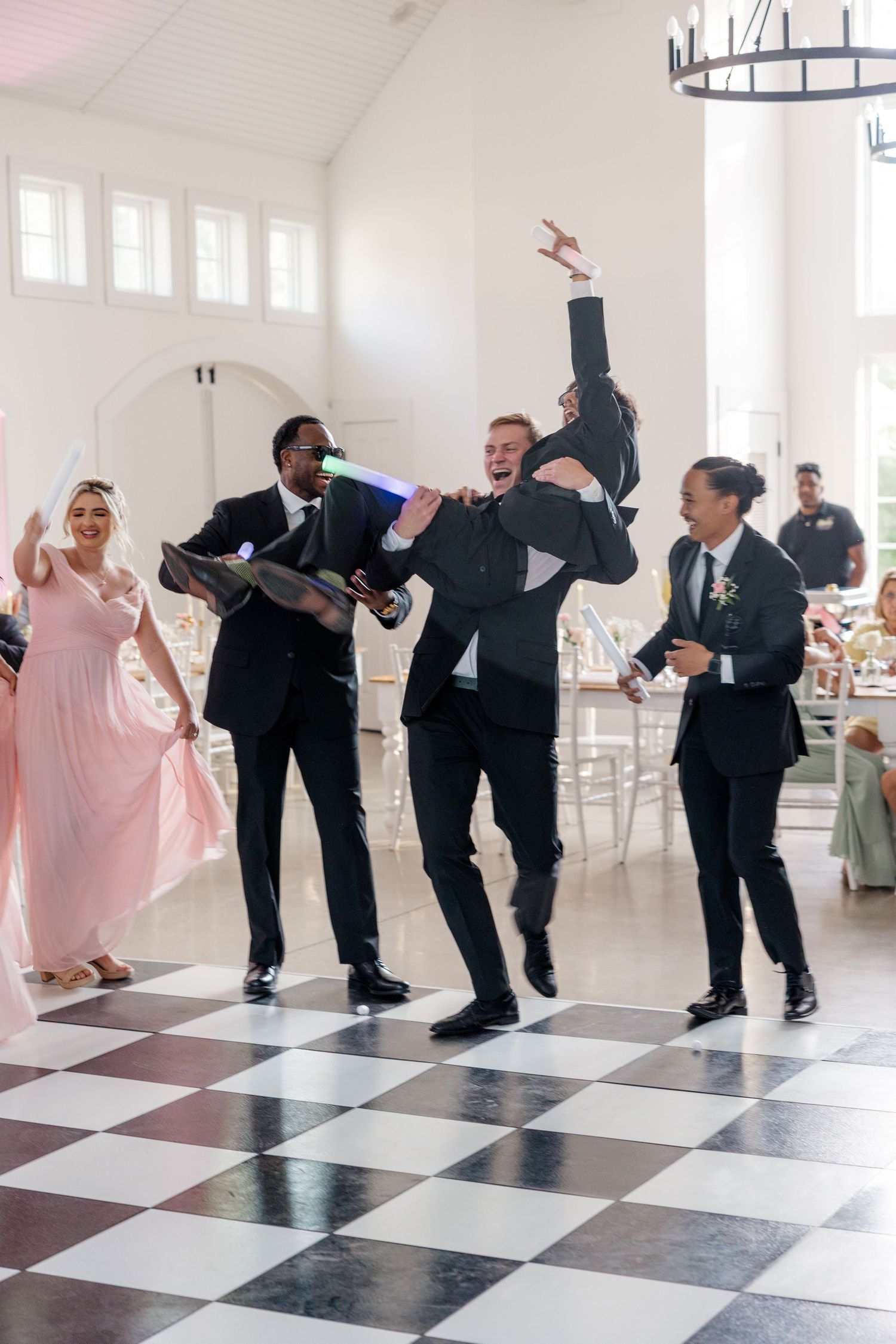Groomsmen dancing and celebrating on black and white checkered dance floor.