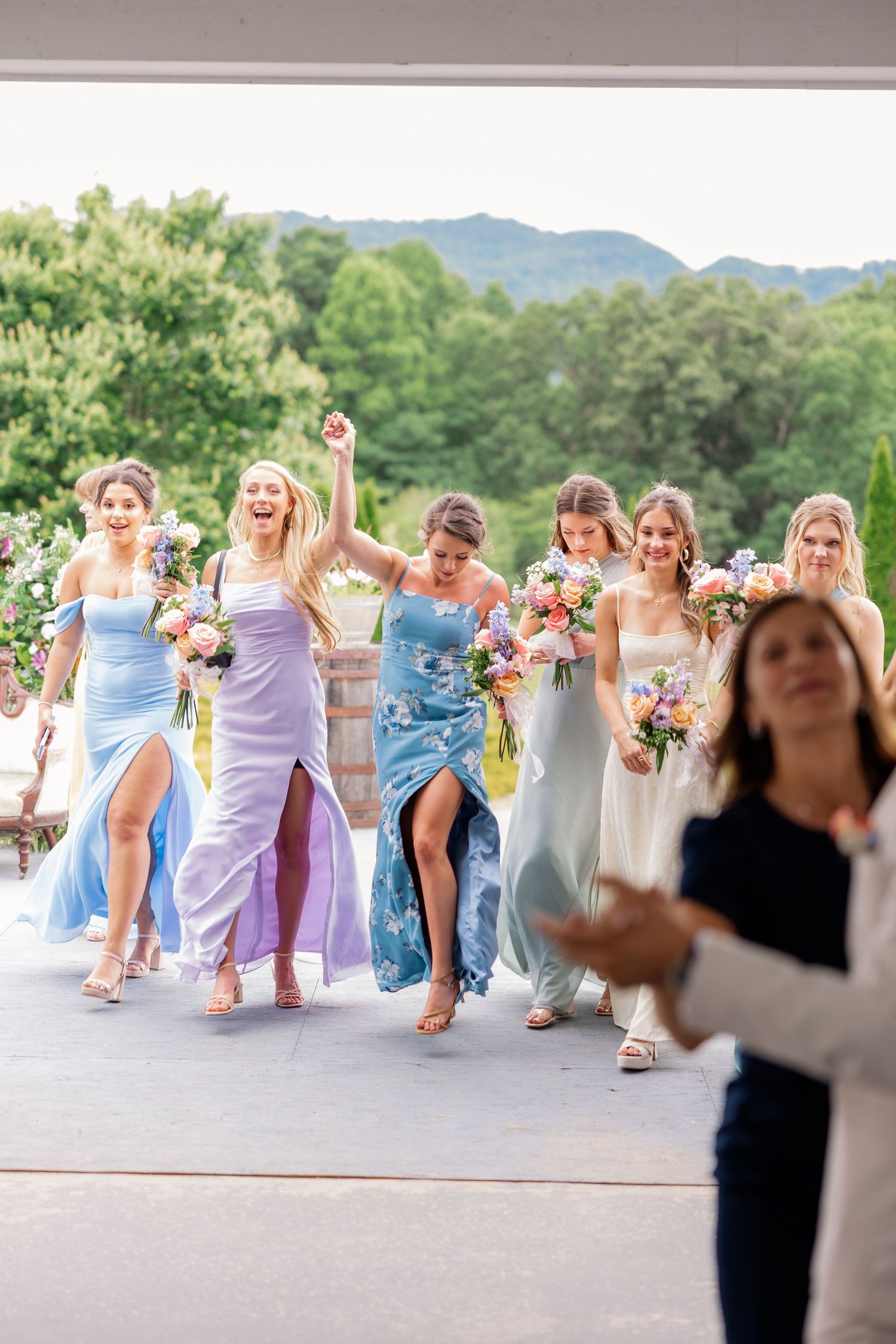 Wedding party in pastel dresses dancing and celebrating on an outdoor patio.