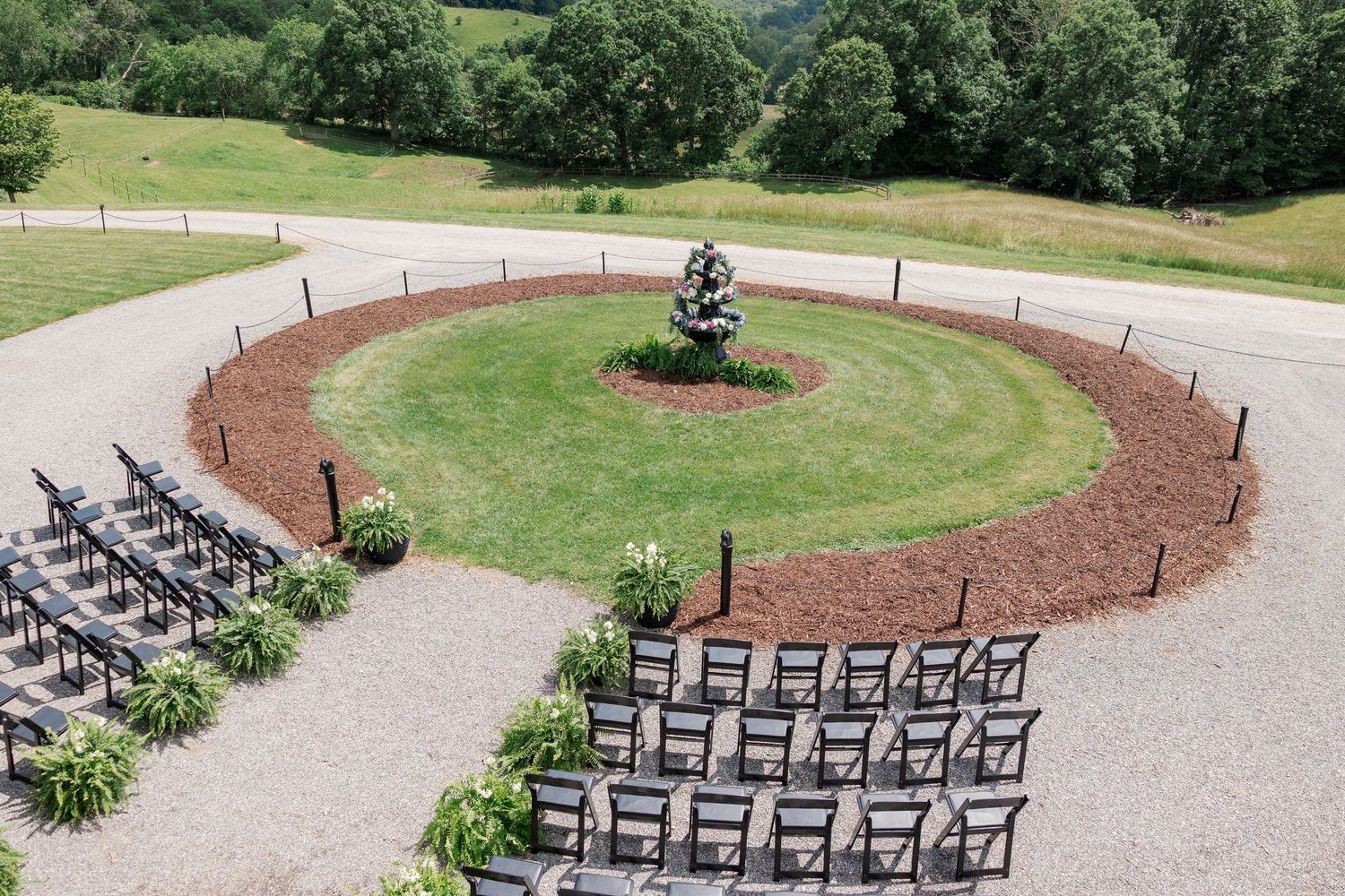 An aerial view of a circular outdoor wedding ceremony setup with rows of chairs arranged around a central focal point.