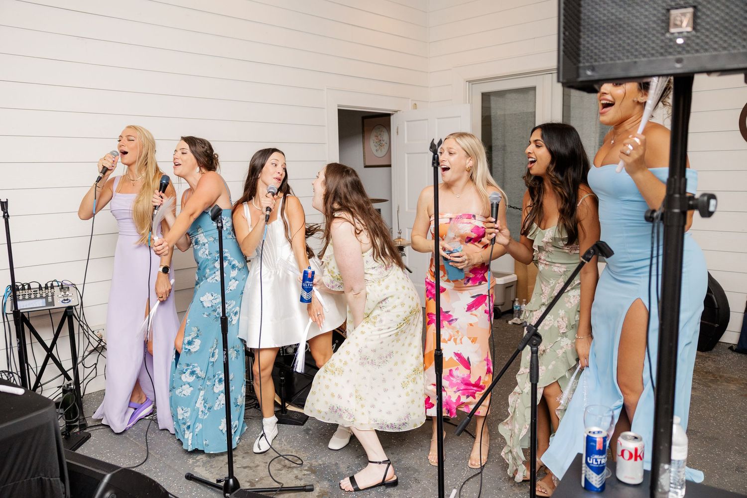 Wedding party dancing and celebrating in pastel dresses against a white wall backdrop.