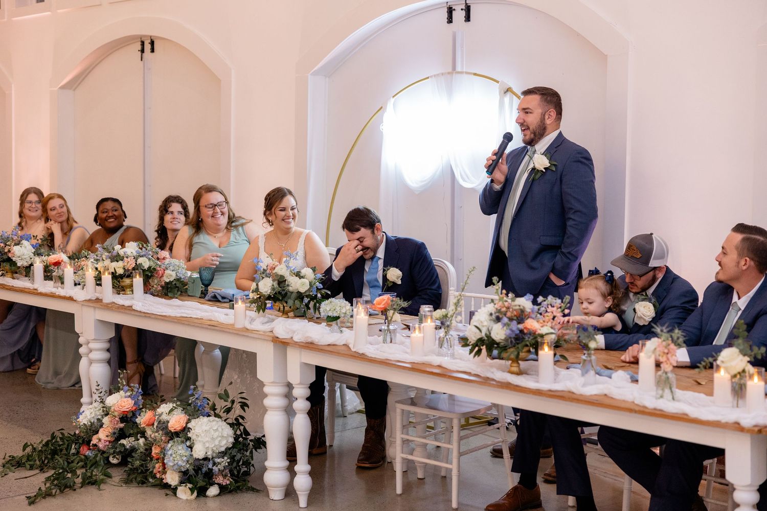 Wedding reception venue with guests seated at elegant white tables under arched ceilings.
