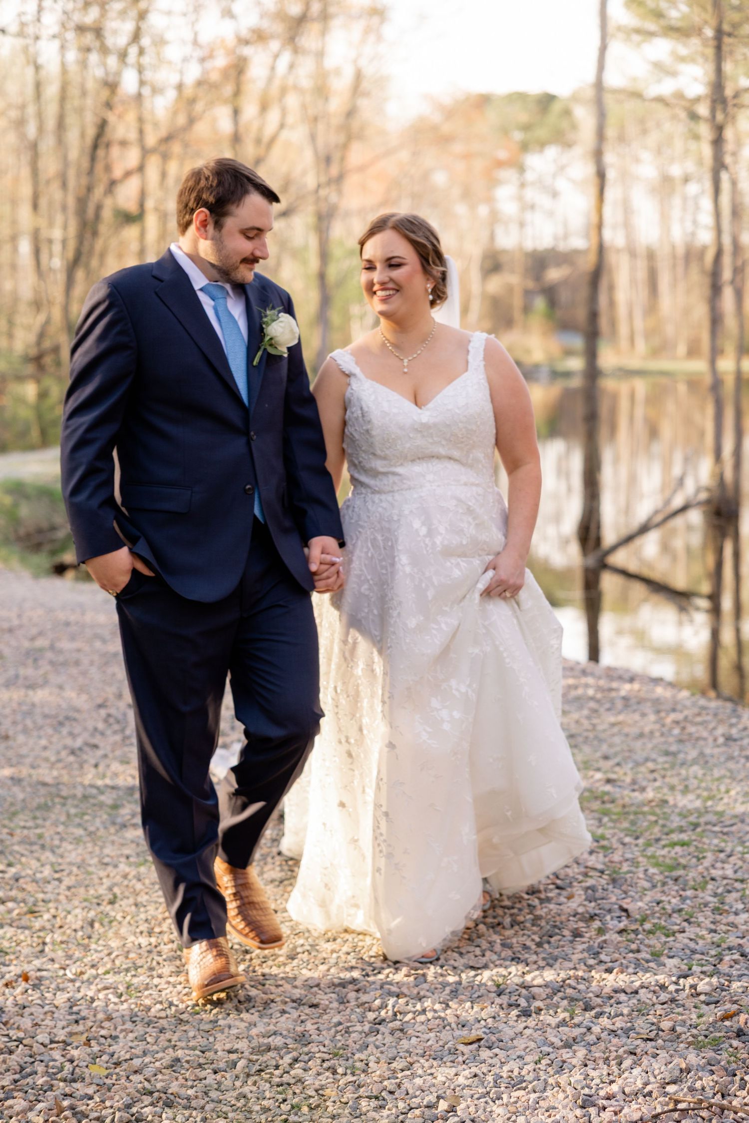 Joyful wedding couple running and laughing together on a gravel path.