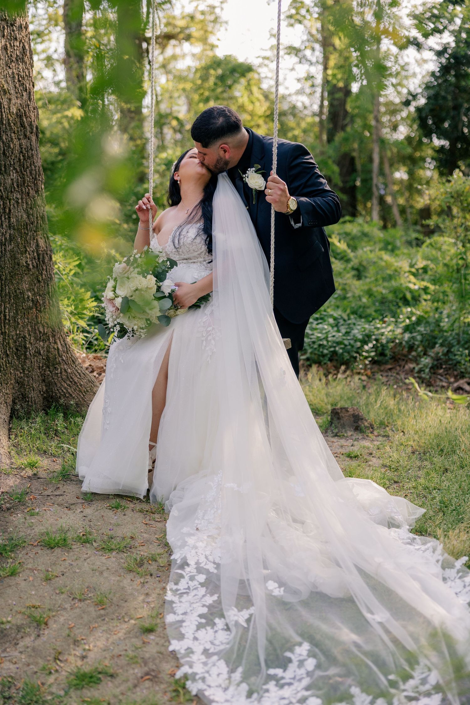 A couple poses for romantic wedding photos among trees with a flowing white dress.