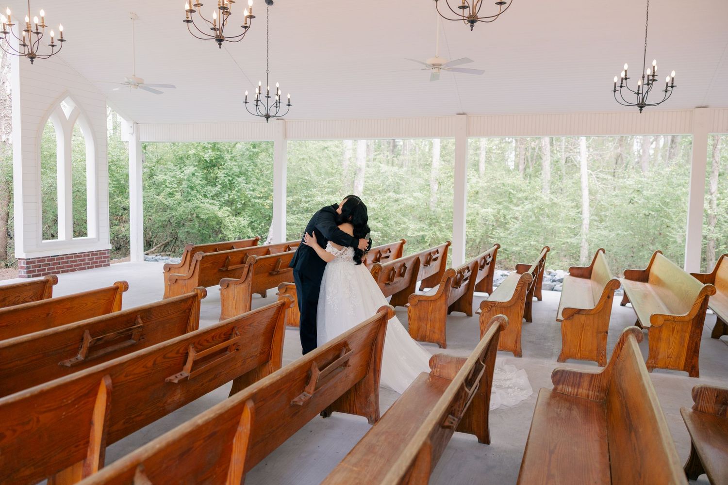 Sunlit chapel interior with wooden pews and chandeliers creating a romantic wedding ceremony setting.