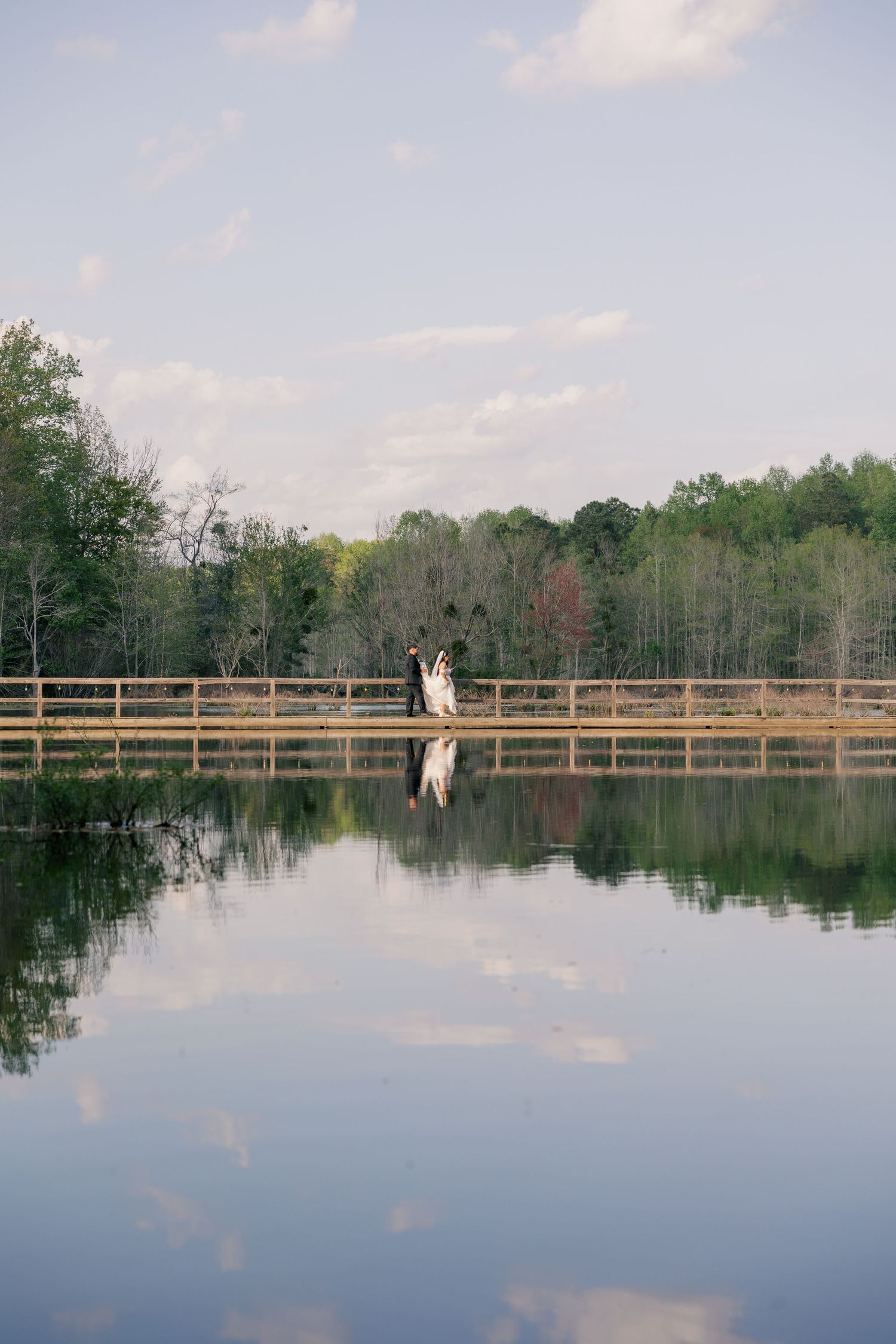 Romantic silhouette of newlyweds on wooden bridge with perfect lake reflection.