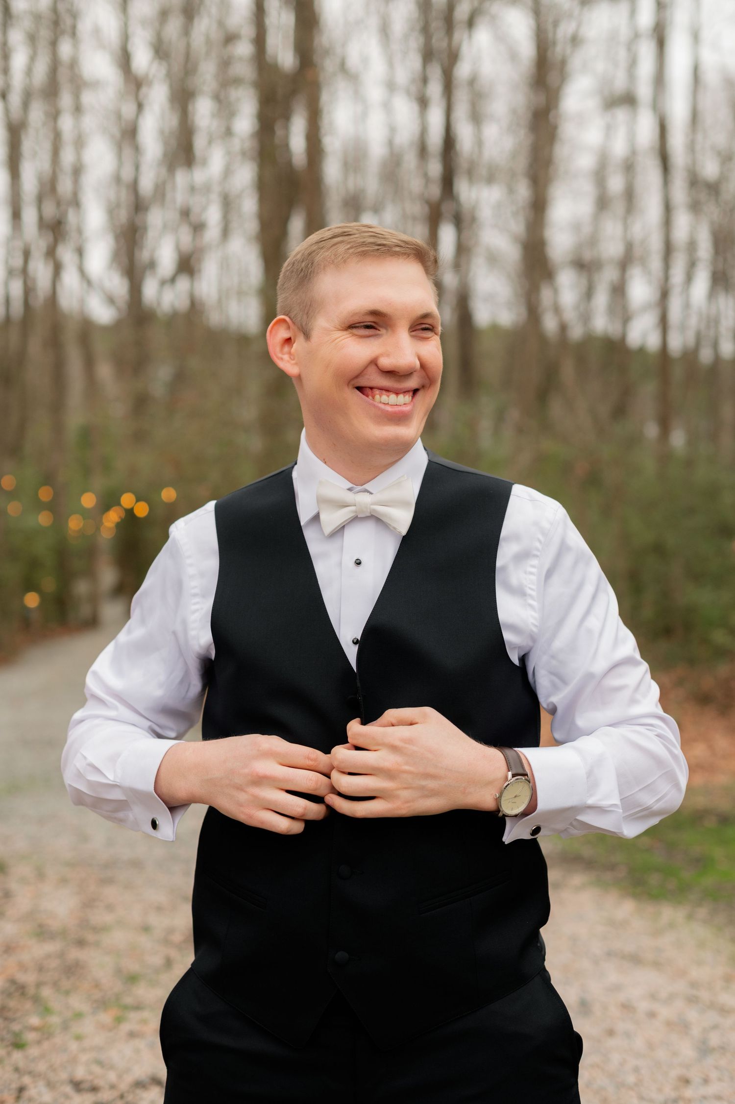 Groom in formal attire laughs joyfully during wedding preparation photos outdoors.