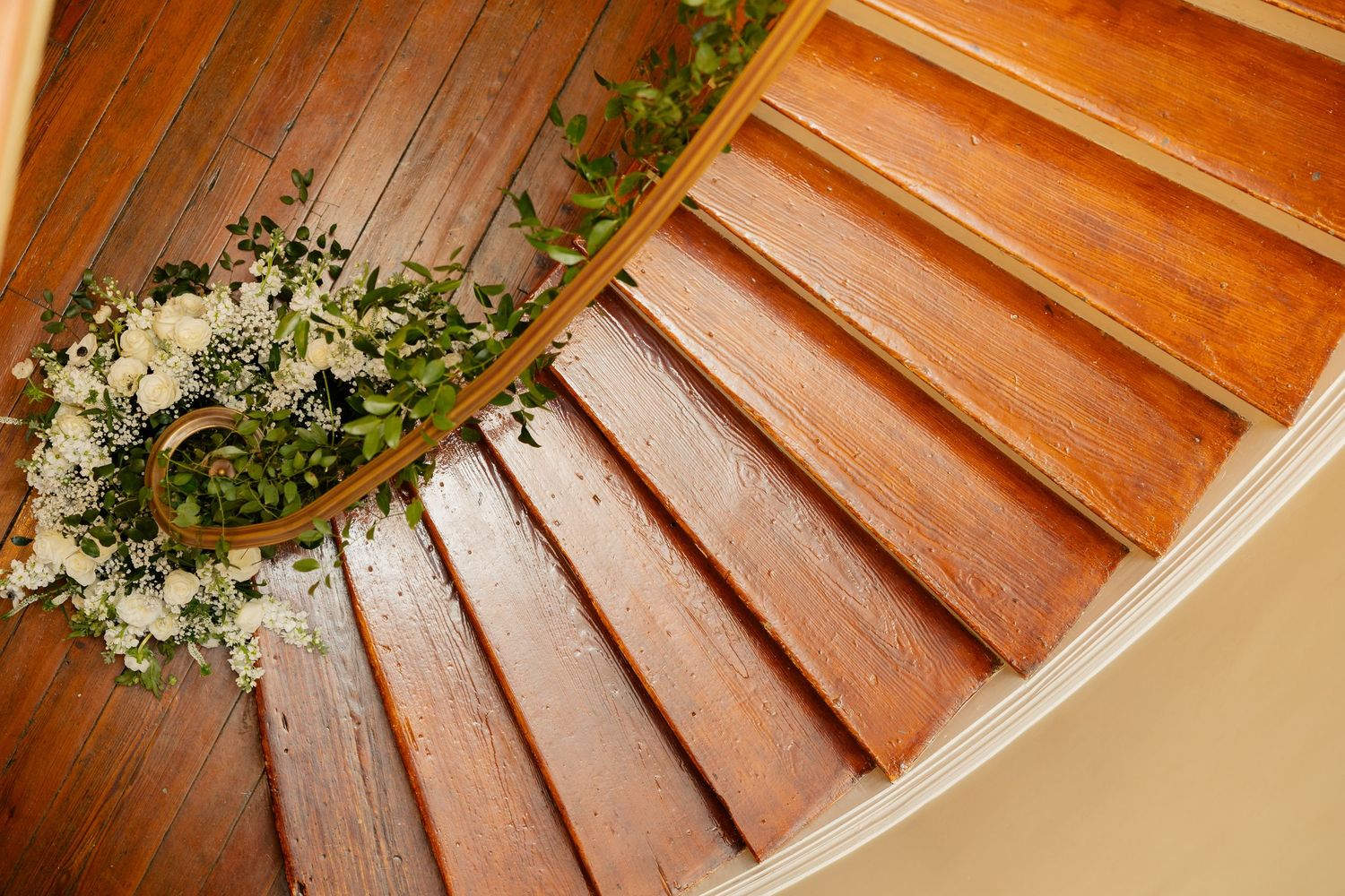 A curved wooden staircase decorated with white floral arrangements at the base.