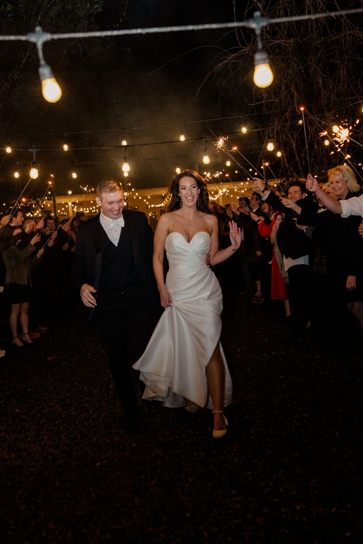 String lights illuminate an outdoor wedding reception as figures dance together on a dark evening.