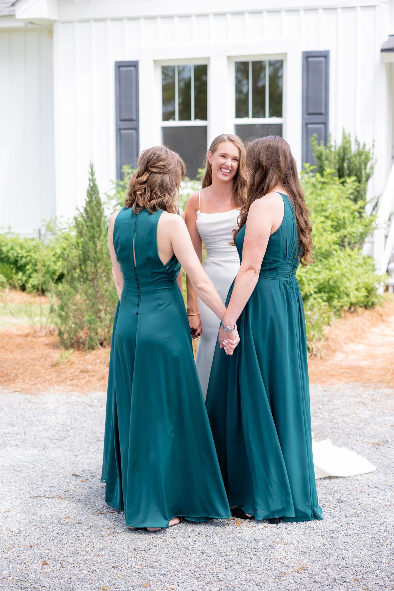 Three women in formal attire stand together outdoors, with two wearing elegant teal bridesmaid dresses.