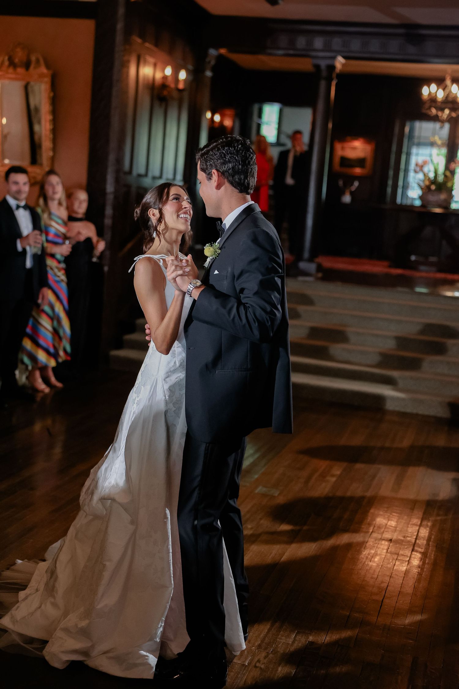 Bride and groom share first dance smiling at each other in grand ballroom wedding reception.