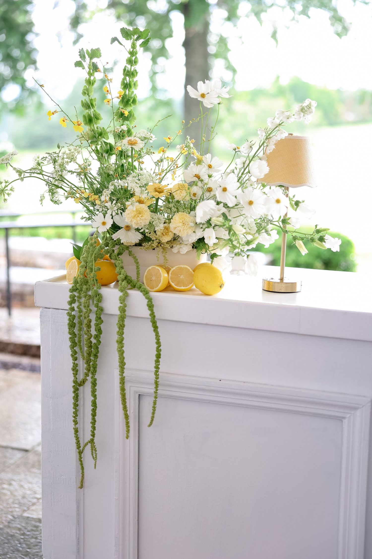 White bar decorated with yellow lemons, white flowers, greenery, and a small gold lamp for a wedding.