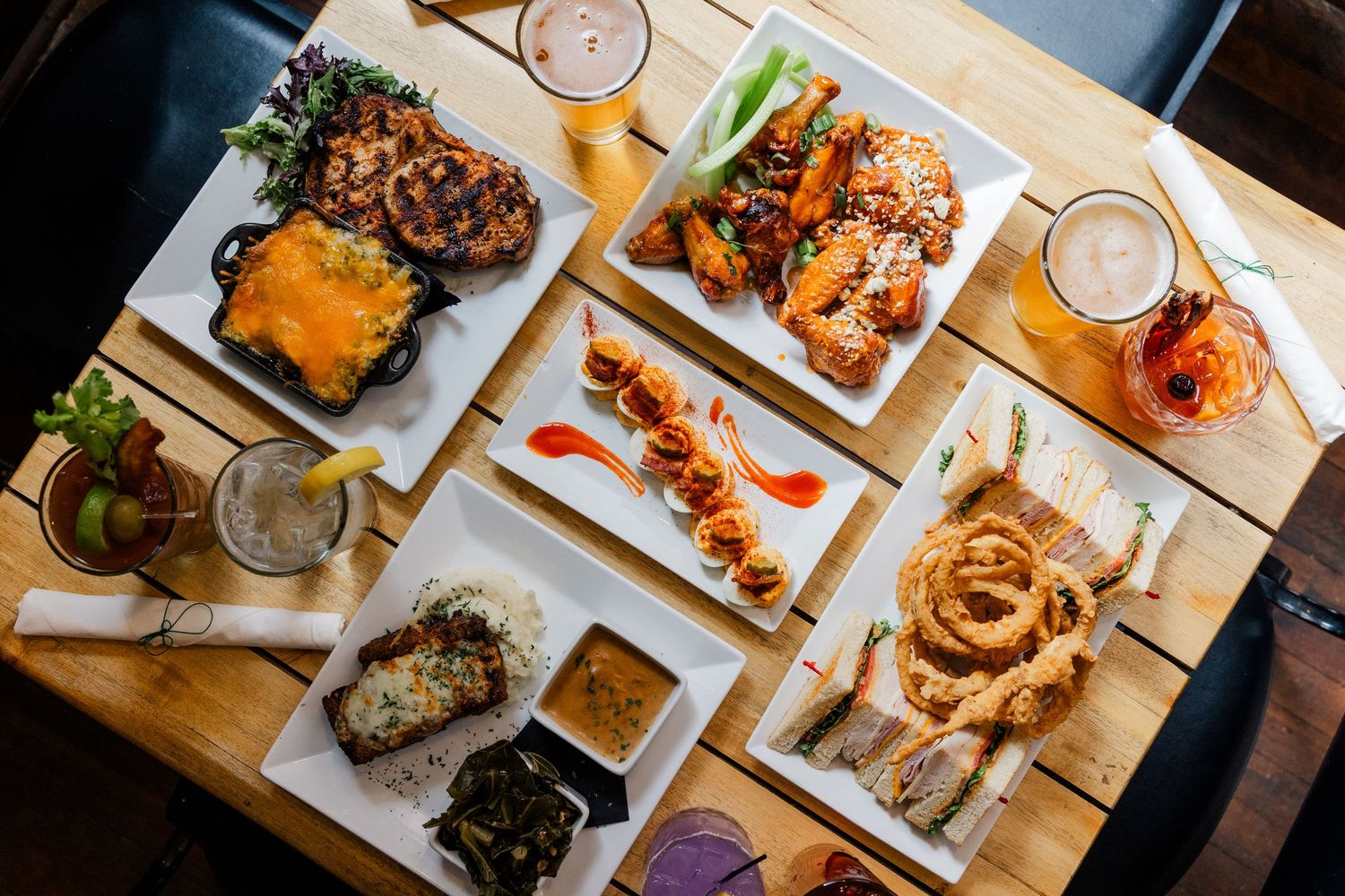 Overhead view of Asian dishes and cocktail drinks arranged on a wooden restaurant table with white plates.