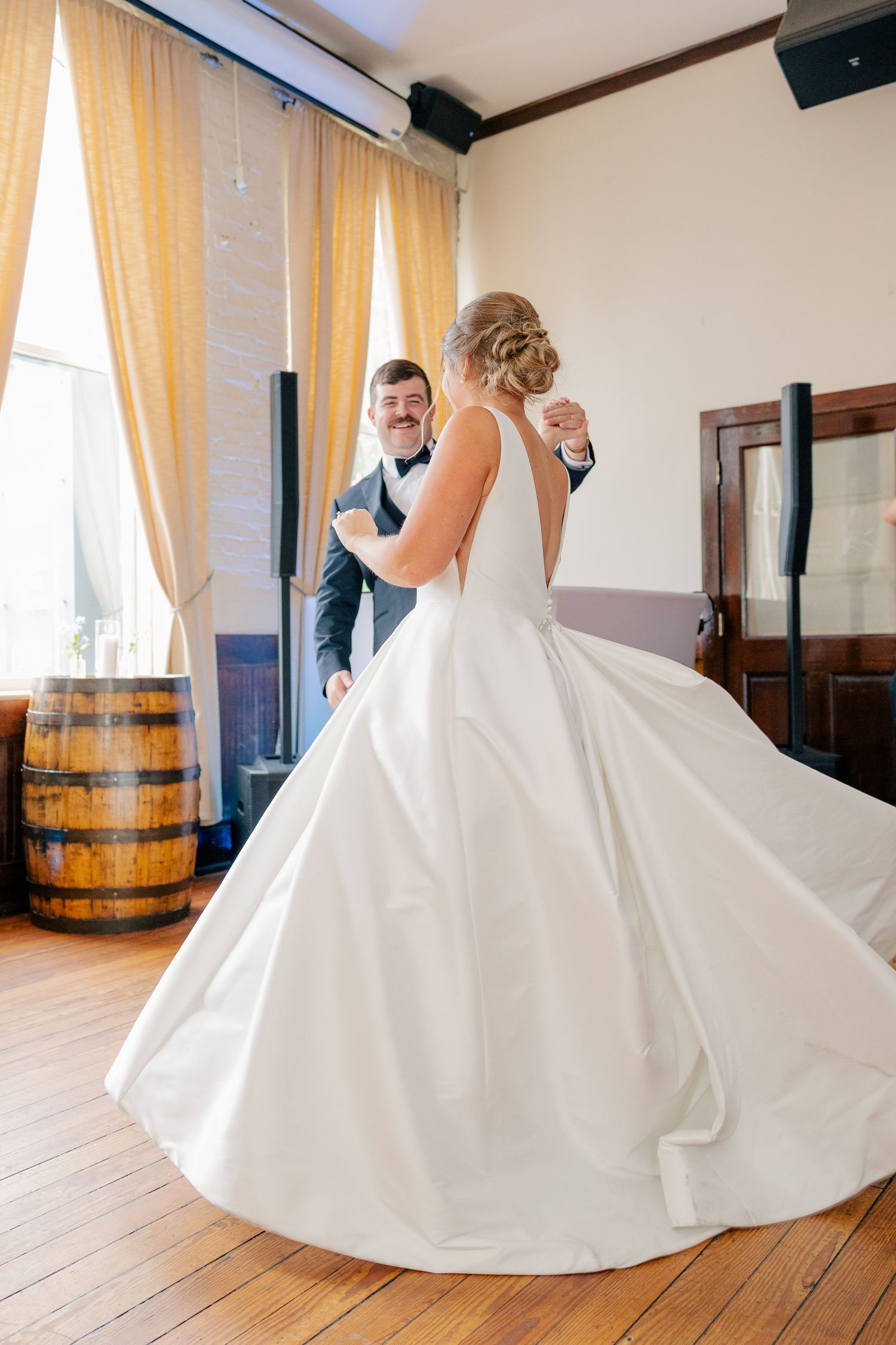 Bride and older gentleman share joyful father-daughter dance in warmly lit rustic reception venue.