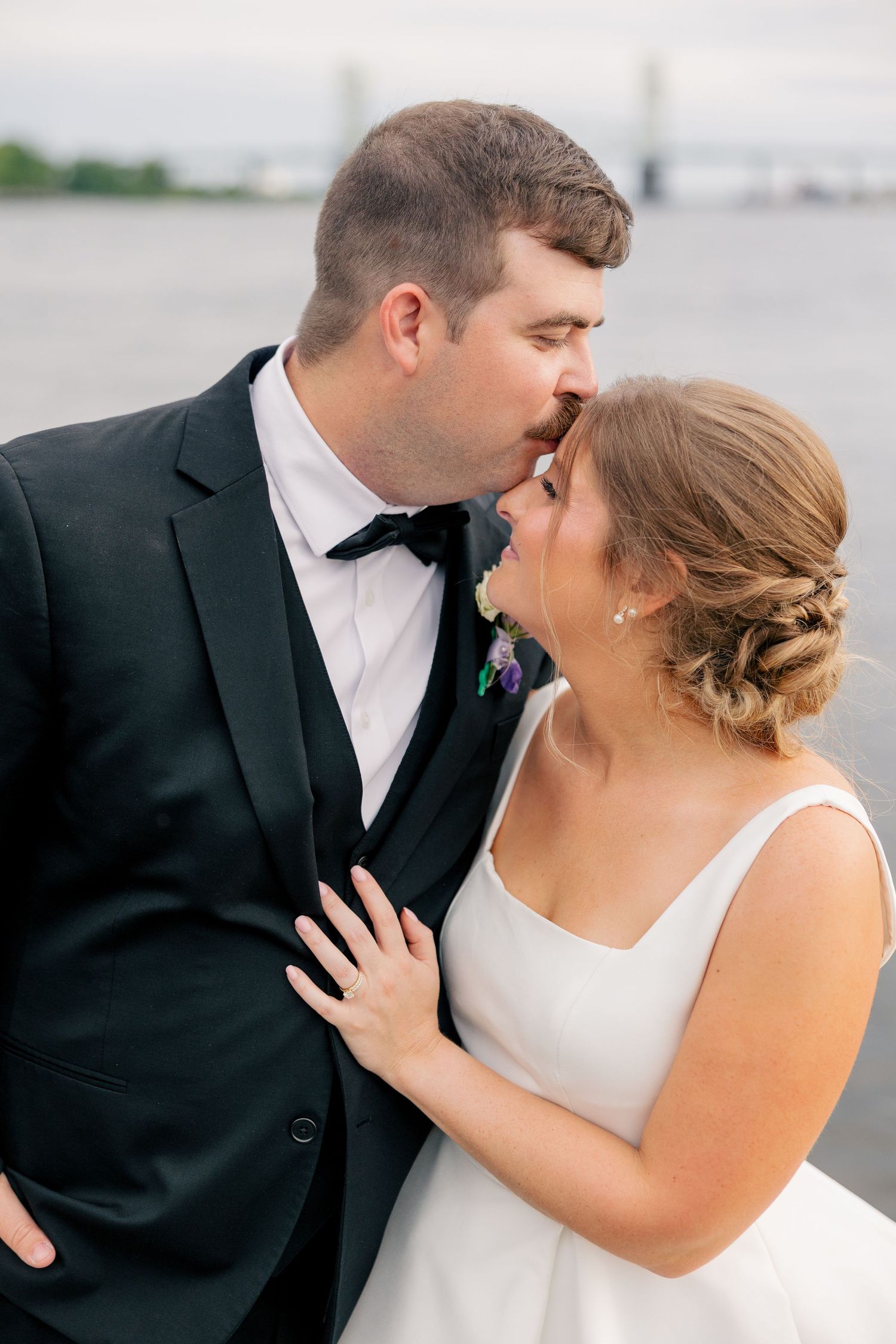 Bride and groom share romantic kiss near waterfront on their wedding day.