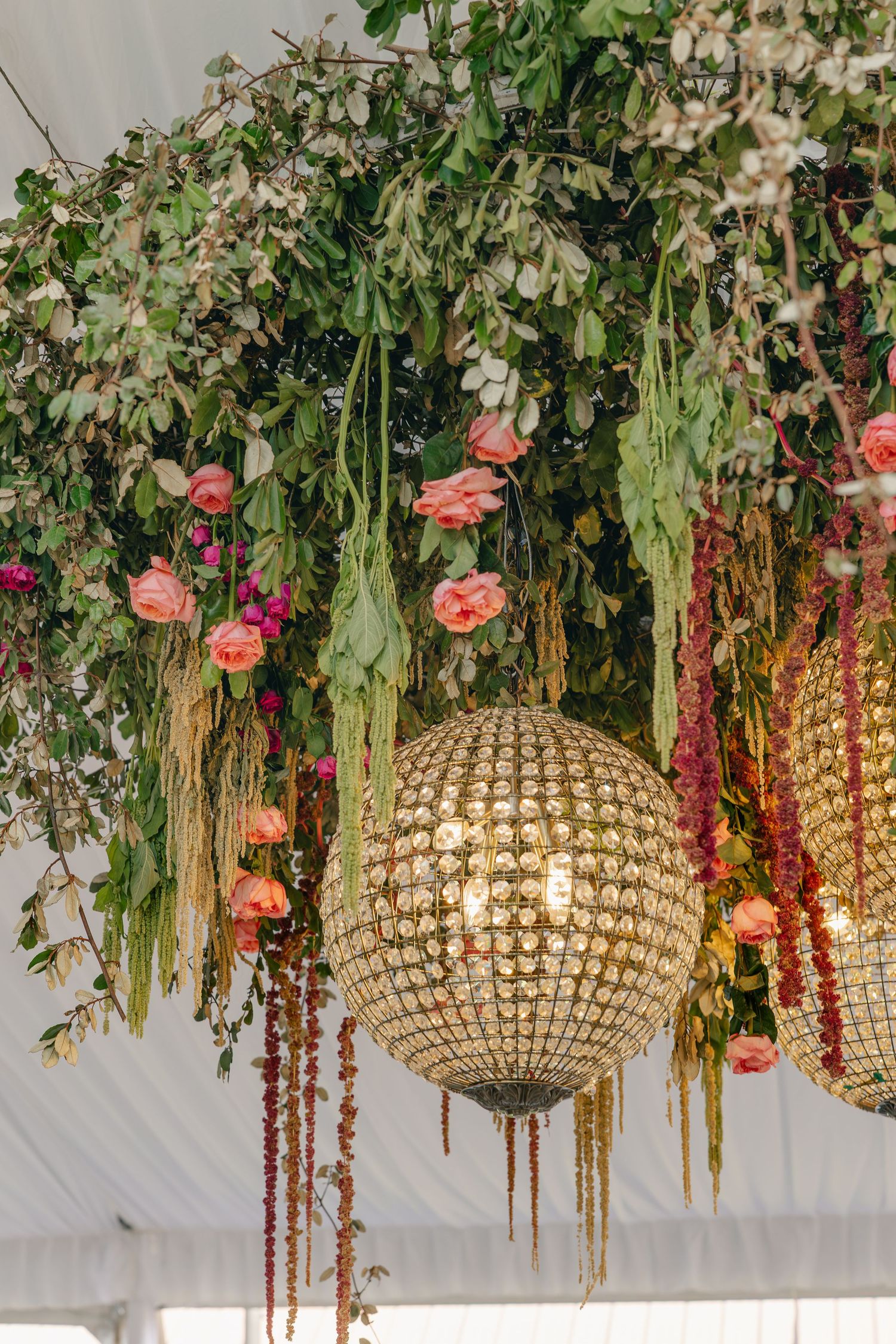 Lush floral ceiling installation with gold disco balls, pink roses, and trailing greenery in a tent.
