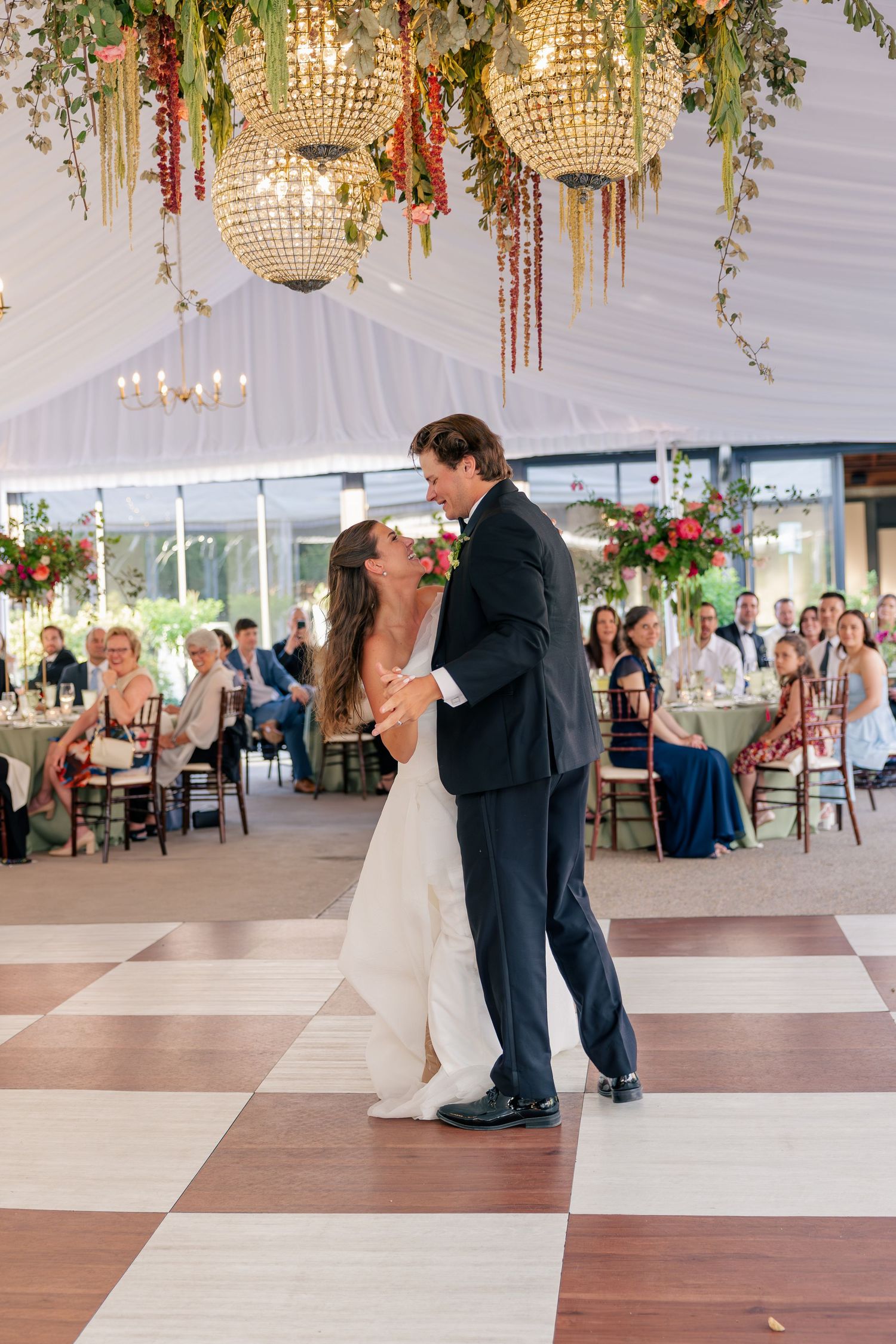 Newlyweds share first dance under glittering globe chandeliers in tented reception venue.