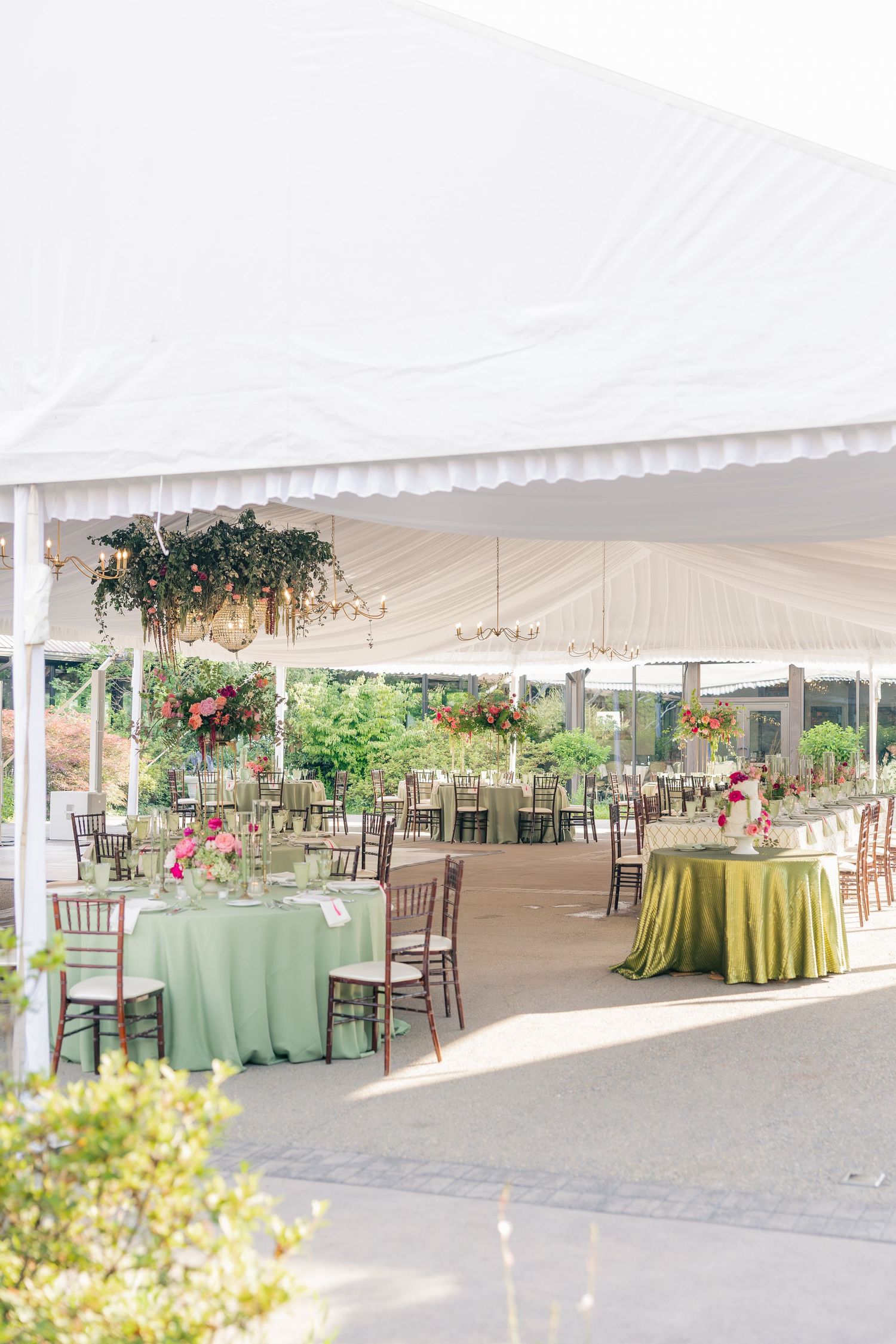 Elegant outdoor wedding reception tent with sage green tablecloths, chiavari chairs, and floral arrangements.