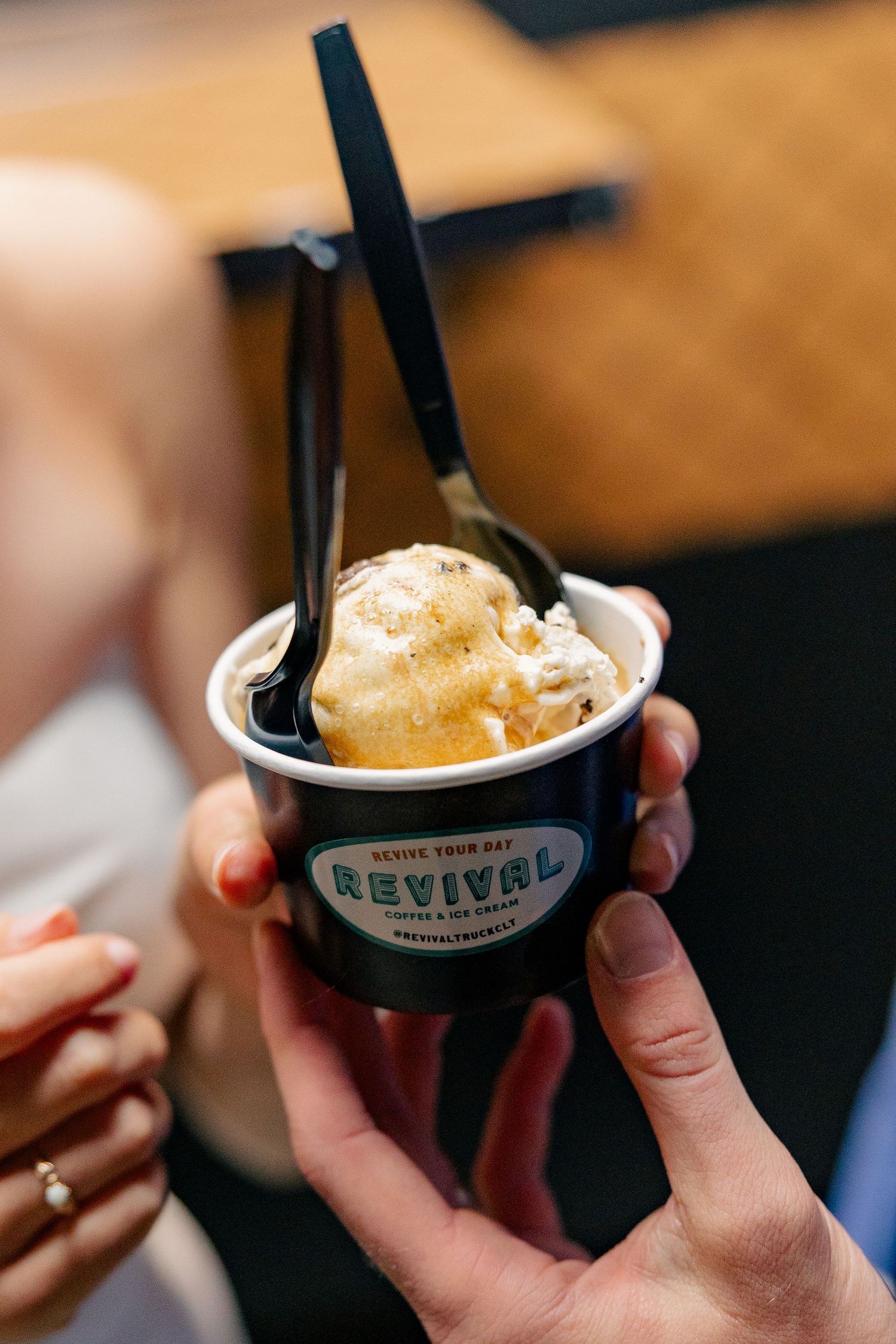 Hand holding a Revival Coffee ice cream cup with a scoop of caramel ice cream and black spoon at a wedding reception.