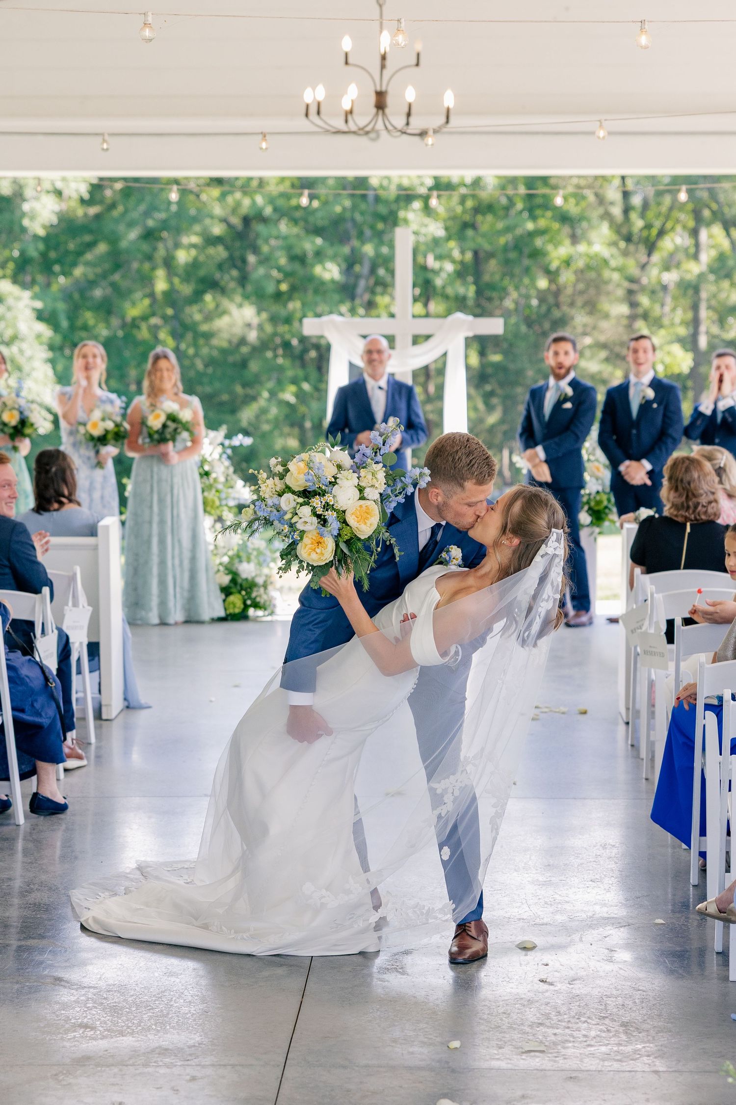 Groom dips bride for romantic kiss during wedding recessional with guests and wedding party watching joyfully.