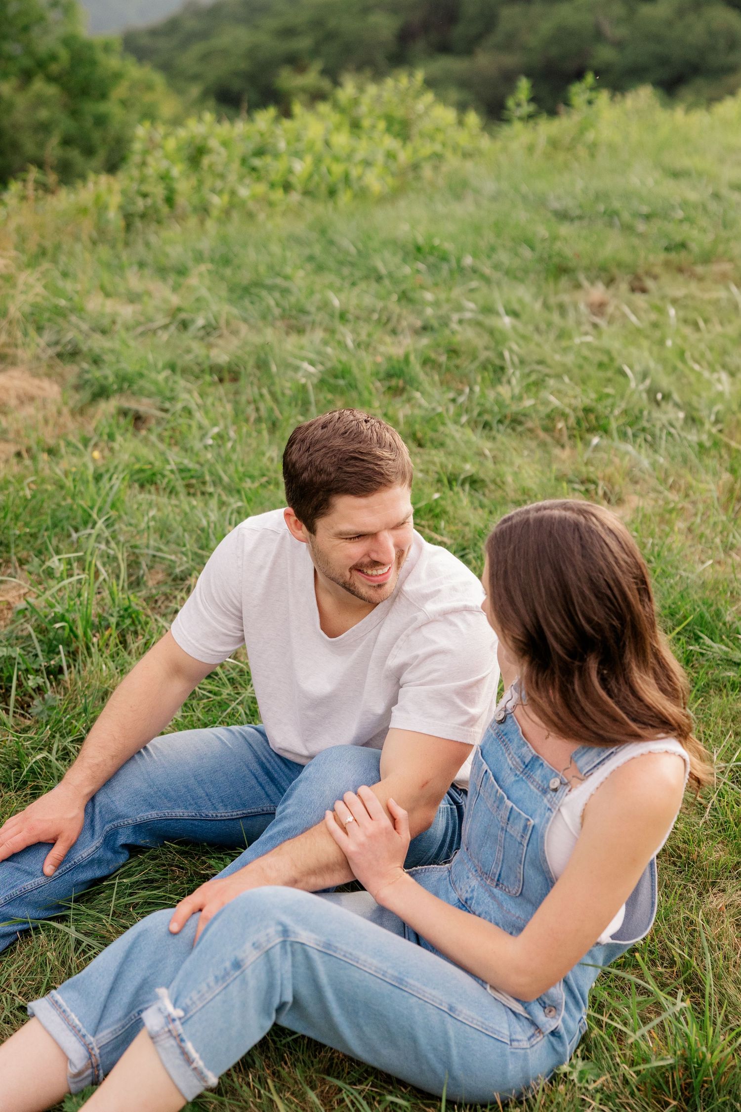Two people lying in the grass share an intimate moment against a mountain backdrop.