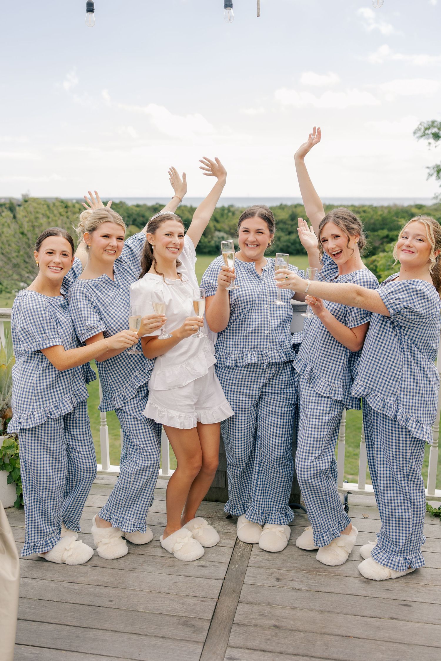 Bride and bridesmaids in blue gingham pajamas celebrating with champagne on outdoor deck.