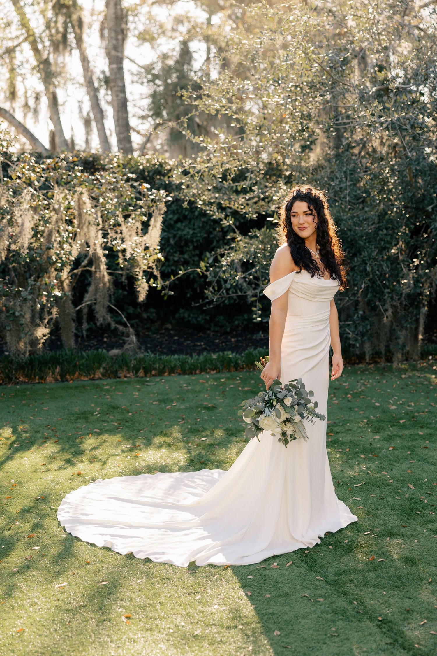 Beautiful outdoor bridal portrait featuring a white mermaid wedding gown with long train in a sunlit garden setting.
