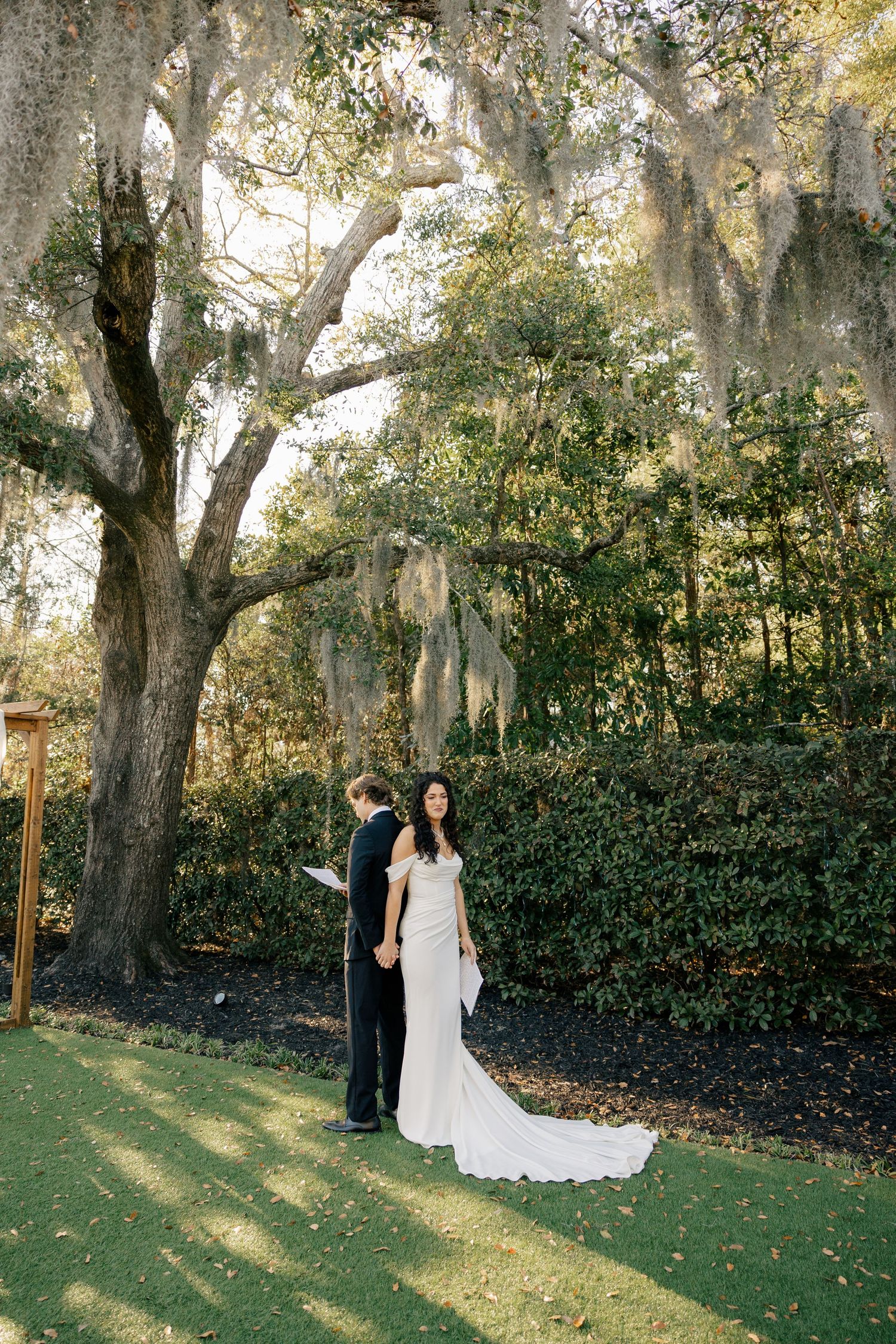 A couple shares an intimate moment under Spanish moss draped trees in a romantic garden setting.