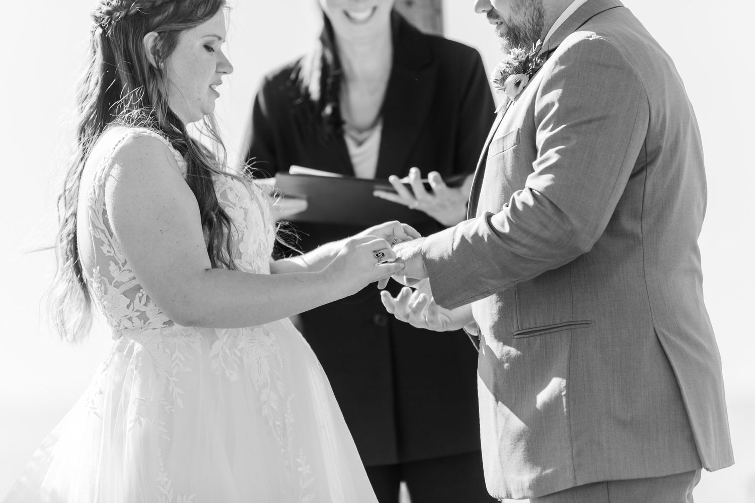Black and white ceremony capture of ring exchange during wedding vows.