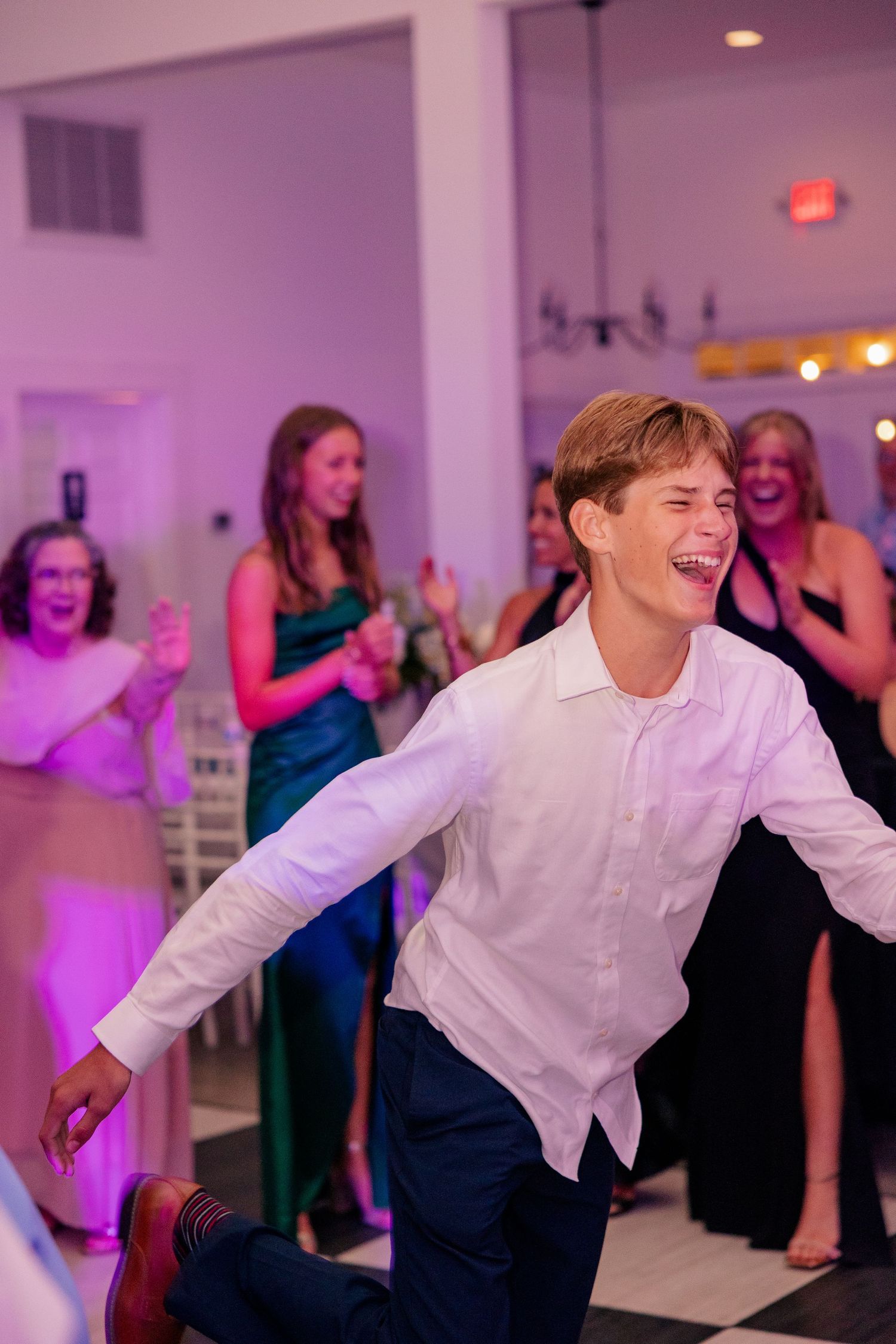 Young man in white shirt laughing and dancing energetically at a wedding reception.