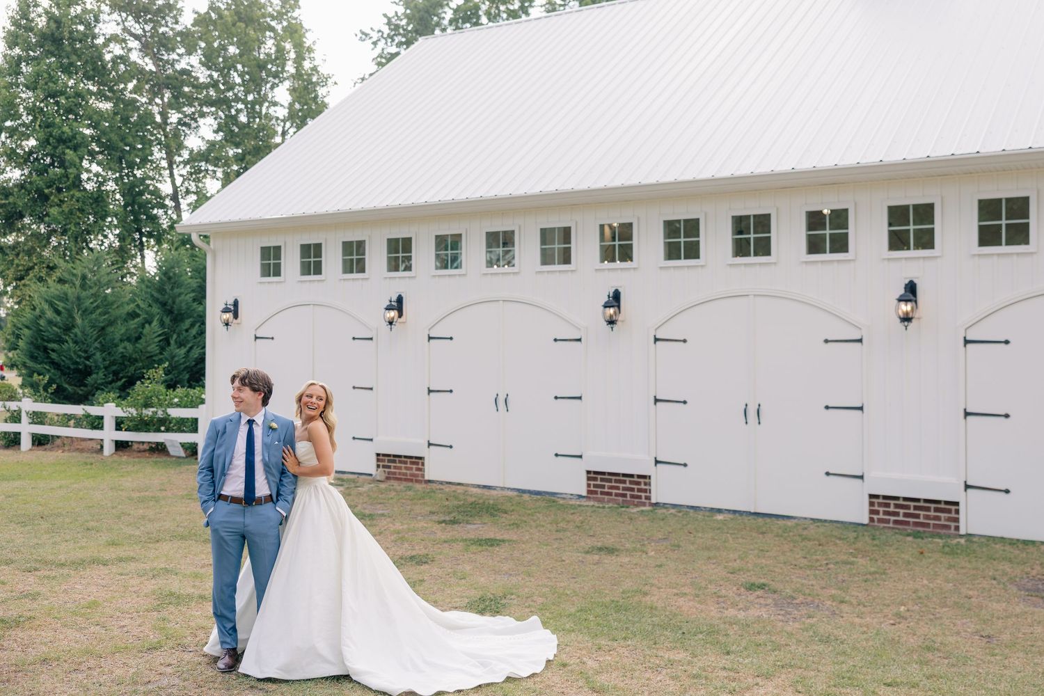 Bride and groom walk hand in hand in front of large white barn wedding venue.