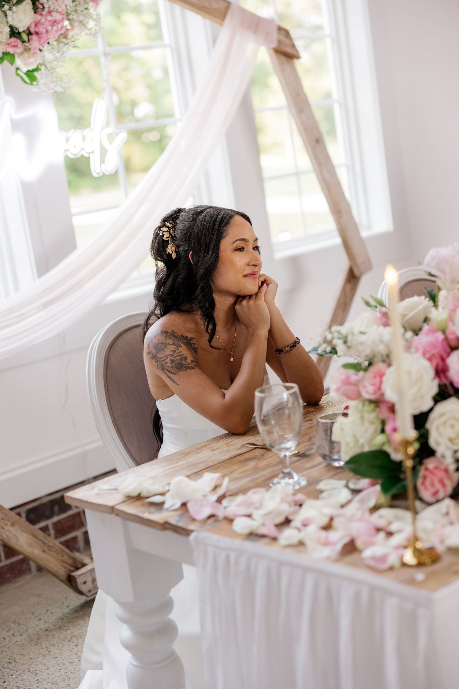 Bride seated at elegantly decorated table with pink floral arrangements and white decor.