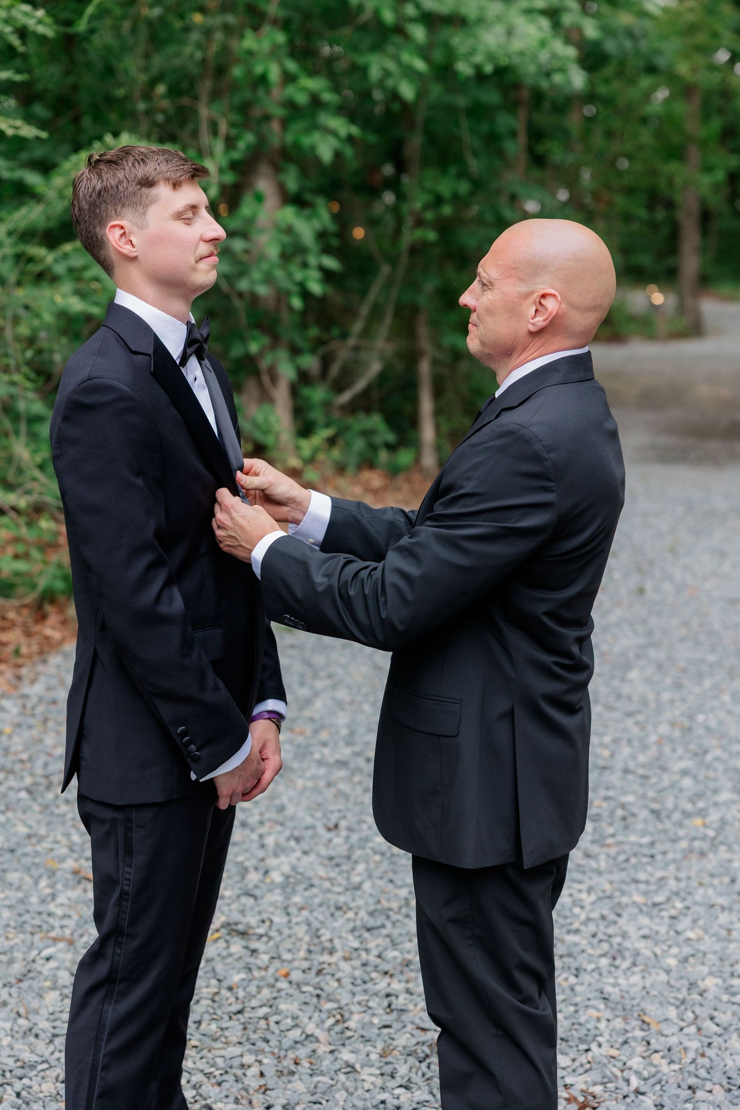Two people in black suits standing together outdoors while adjusting formal attire.