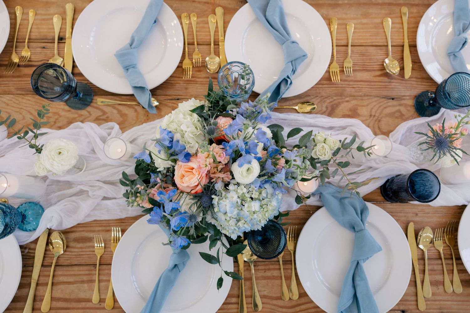 Wedding table setting with blue marbled plates, gold flatware and a centerpiece of blue and peach flowers.