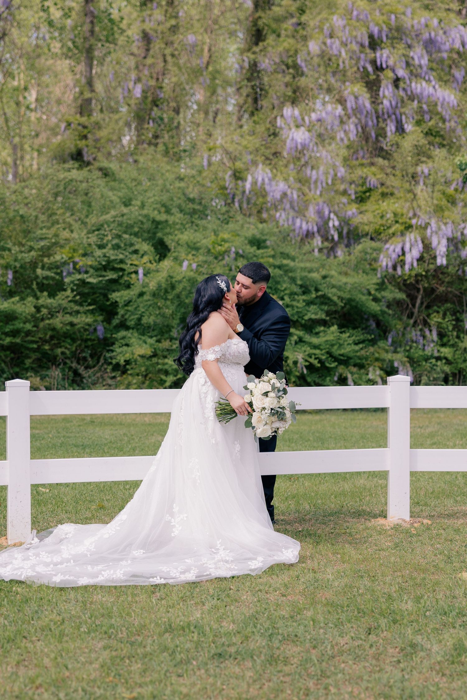 Romantic wedding photos taken against a white fence with blooming wisteria in the background.
