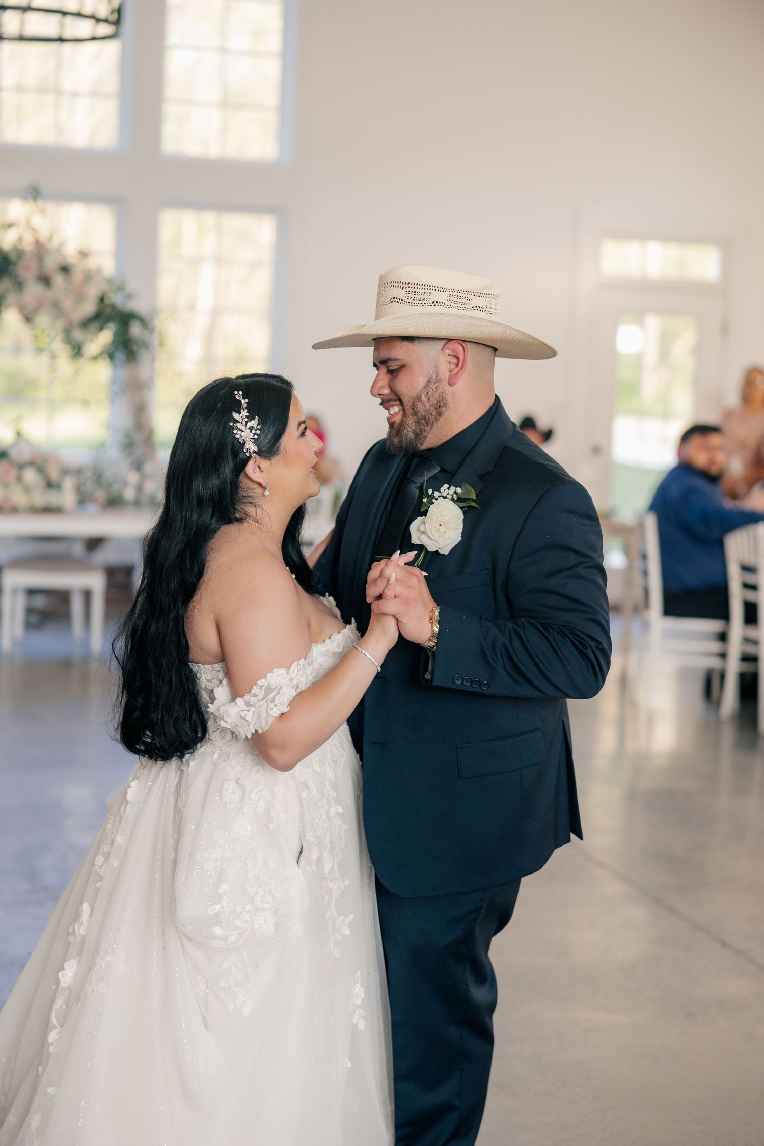 A couple sharing an intimate dance moment in an elegant indoor venue with the groom wearing a western hat.