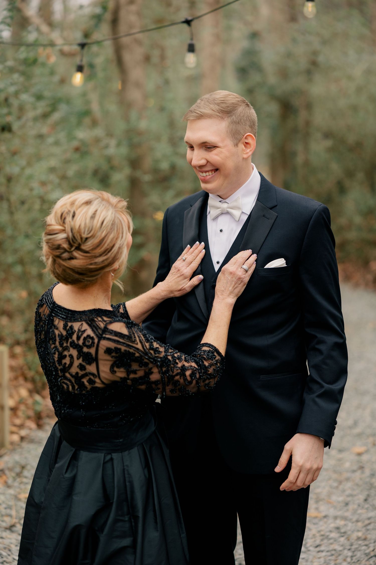 A touching moment between loved ones during formal wedding portraits on a tree-lined gravel path.