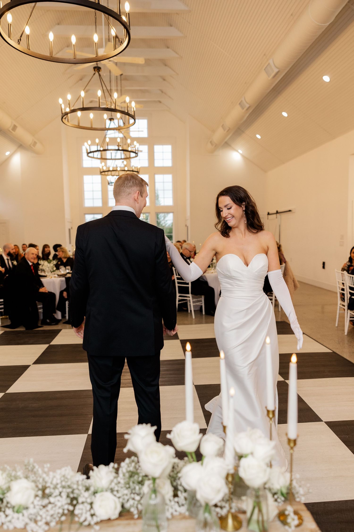 Elegant wedding reception venue with chandeliers and white floral centerpieces during first dance.