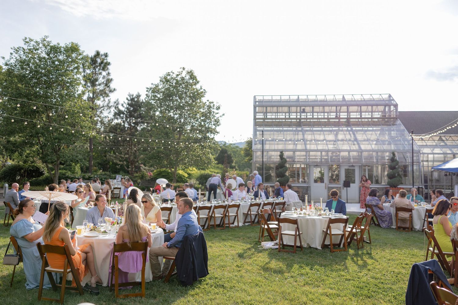 Outdoor wedding reception with guests dining at tables under open sky.