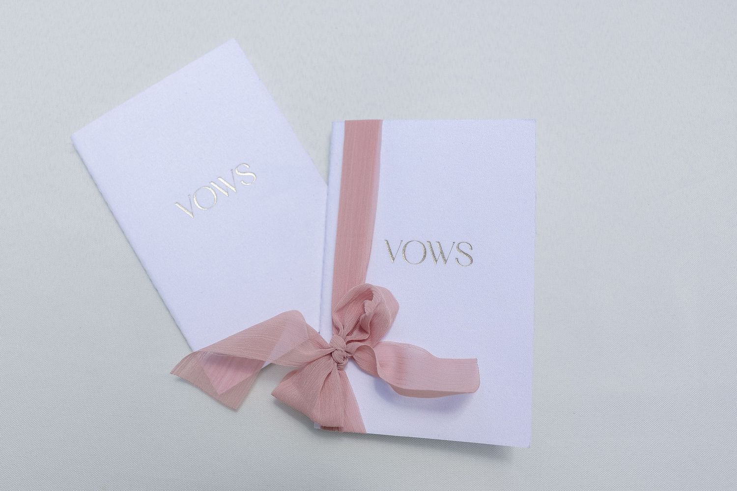 White wedding invitation cards with delicate pink ribbon bows arranged in a minimalist style.